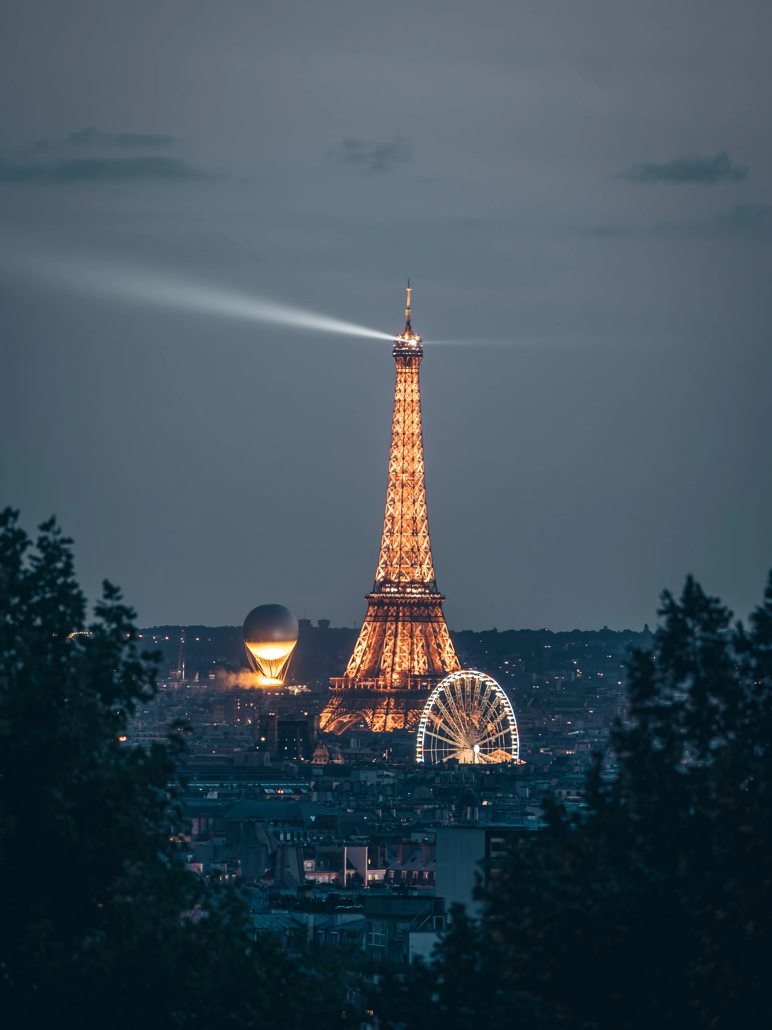 Tour Eiffel illuminée la nuit, avec la vasque olympique, la grande roue et un ciel dégagé en arrière-plan.