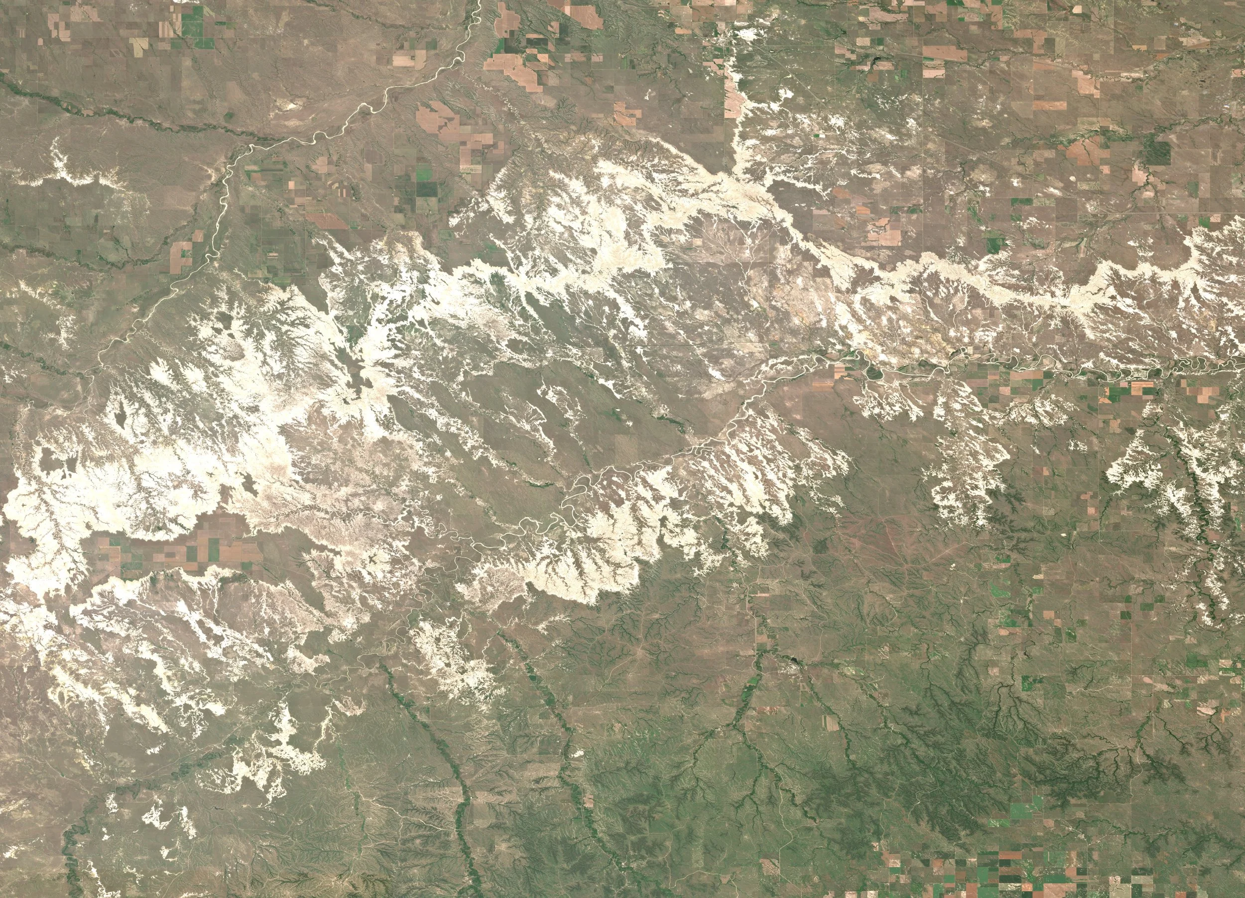 Satellite image of Badlands National Park, with martian-like terrain, winding rivers, and surrounding dry regions with patches of green farmland.