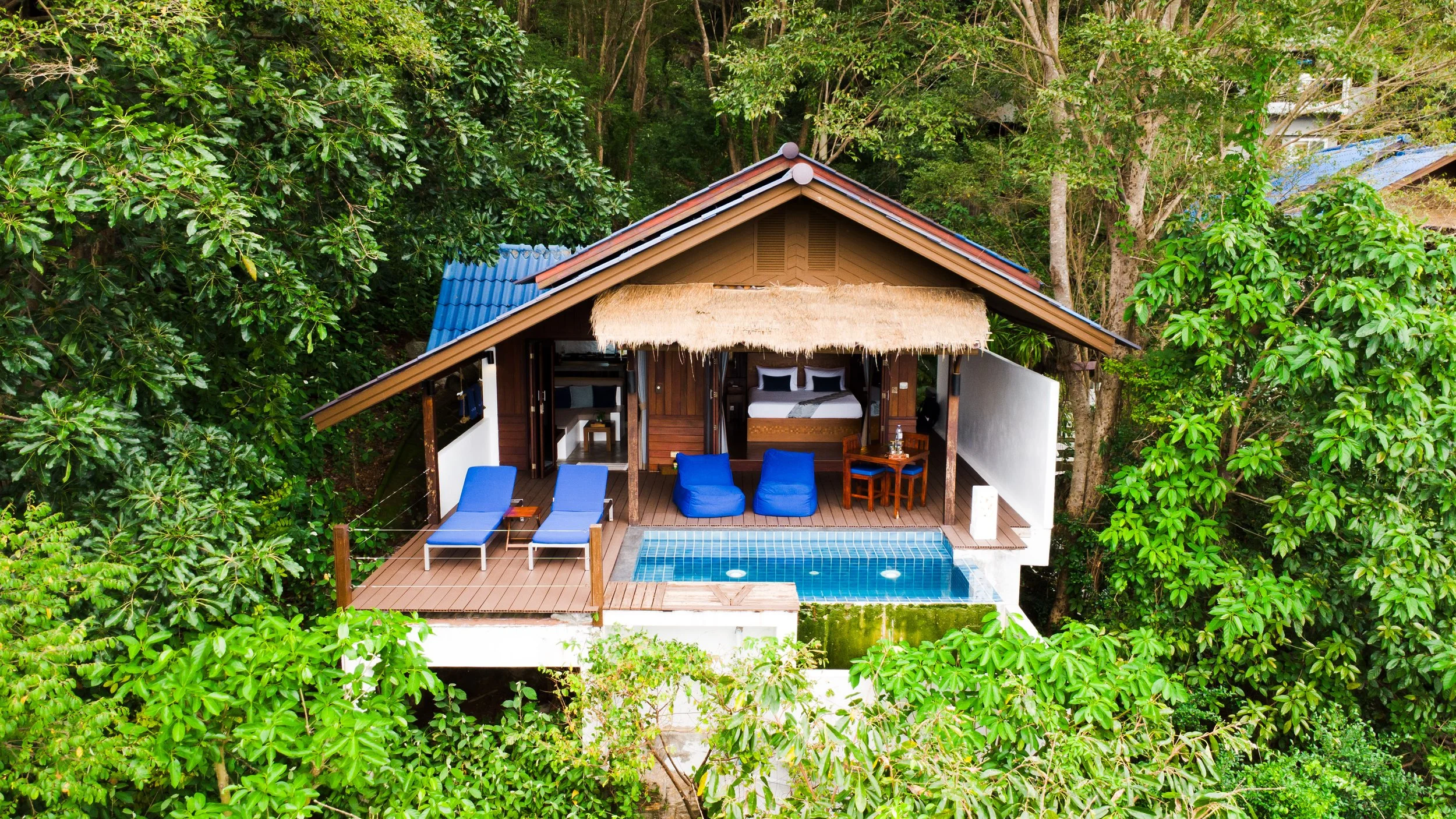 Villa perchée dans la forêt tropicale avec terrasse, piscine, chaises longues, et coin repas.