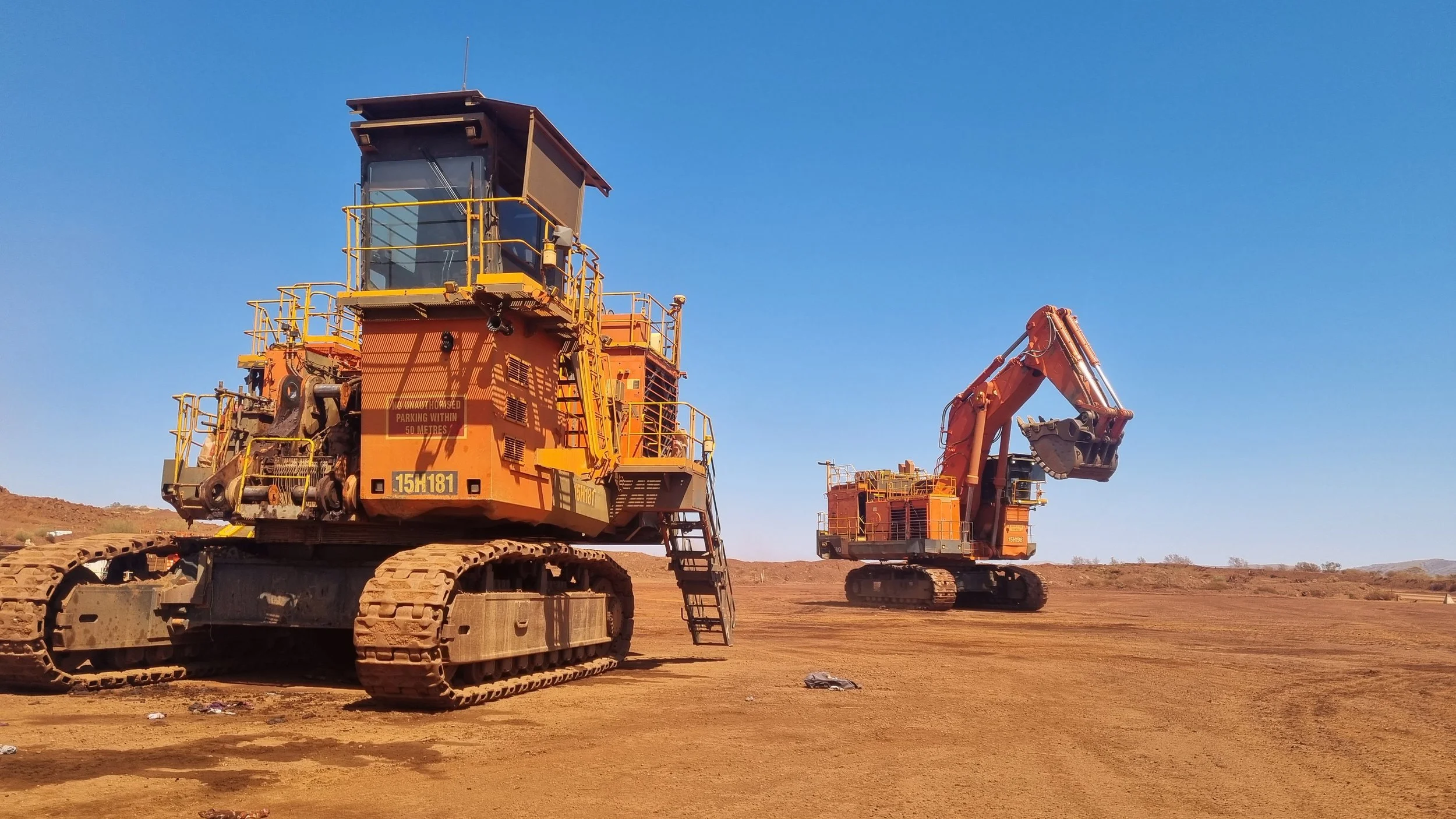Two large orange excavators working on a dirt construction site under a clear blue sky.