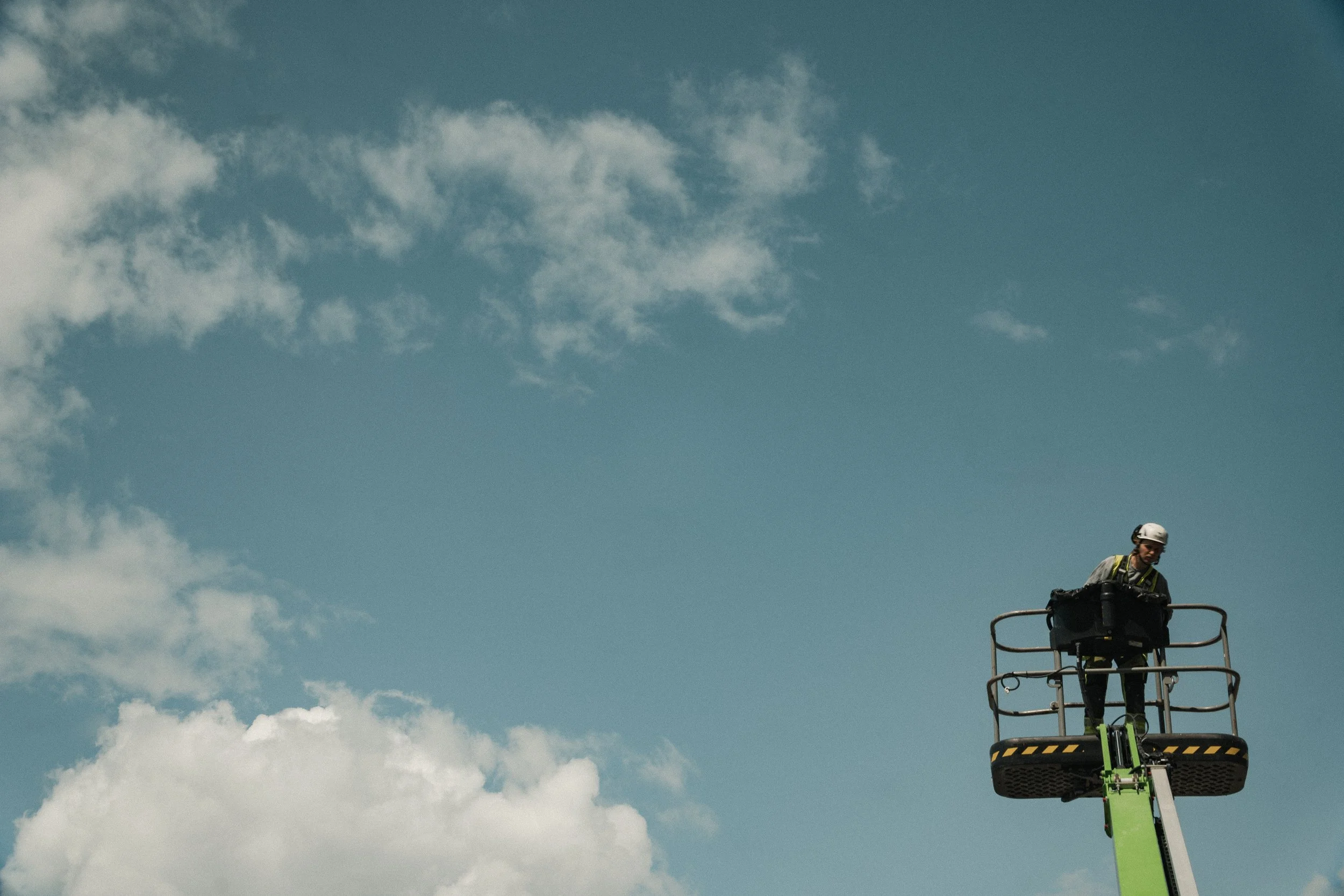 En person står i en lift högt upp mot en blå himmel med några vita moln.