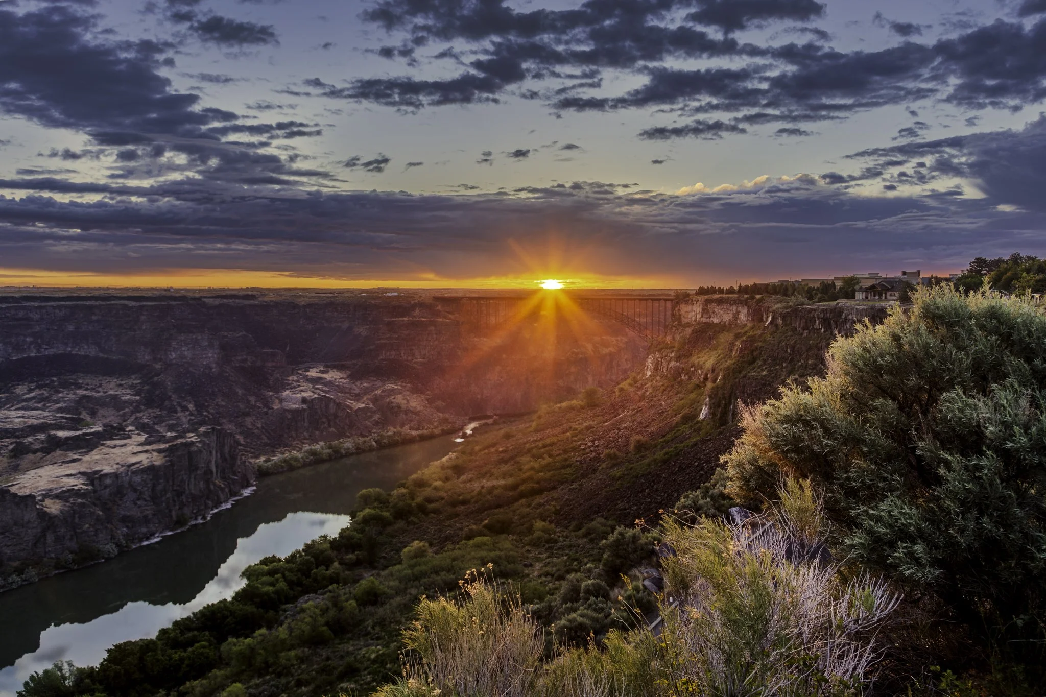 The sun crests the canyon rim and Perrine Bridge as clouds begin to break up after a stormy evening.
