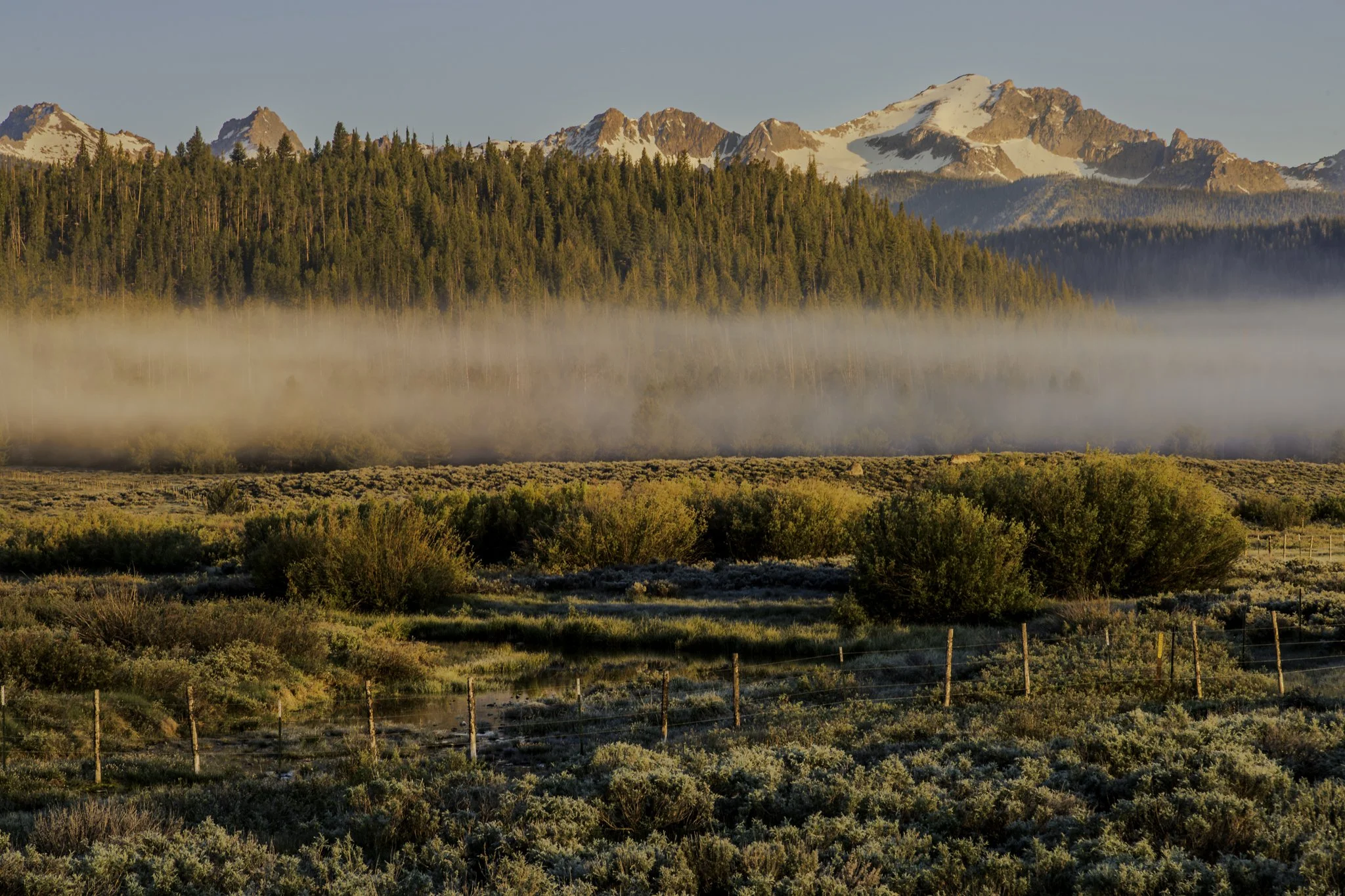 The sunrise on an early June morning lights up the Sawtooth range and fog over Pettit Lake, thawing the frozen valley