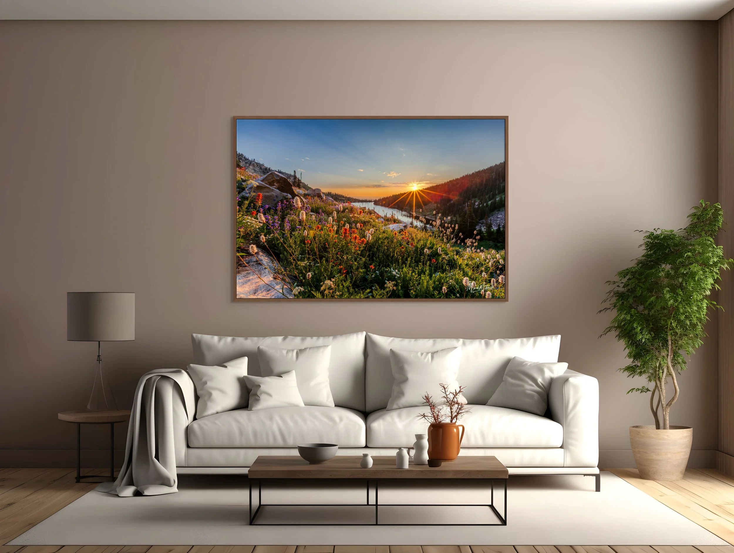 Living room with a white sofa, a wooden coffee table with decorative vases, a potted plant, a floor lamp, and a framed landscape painting of a sunset over a mountainous river scene.