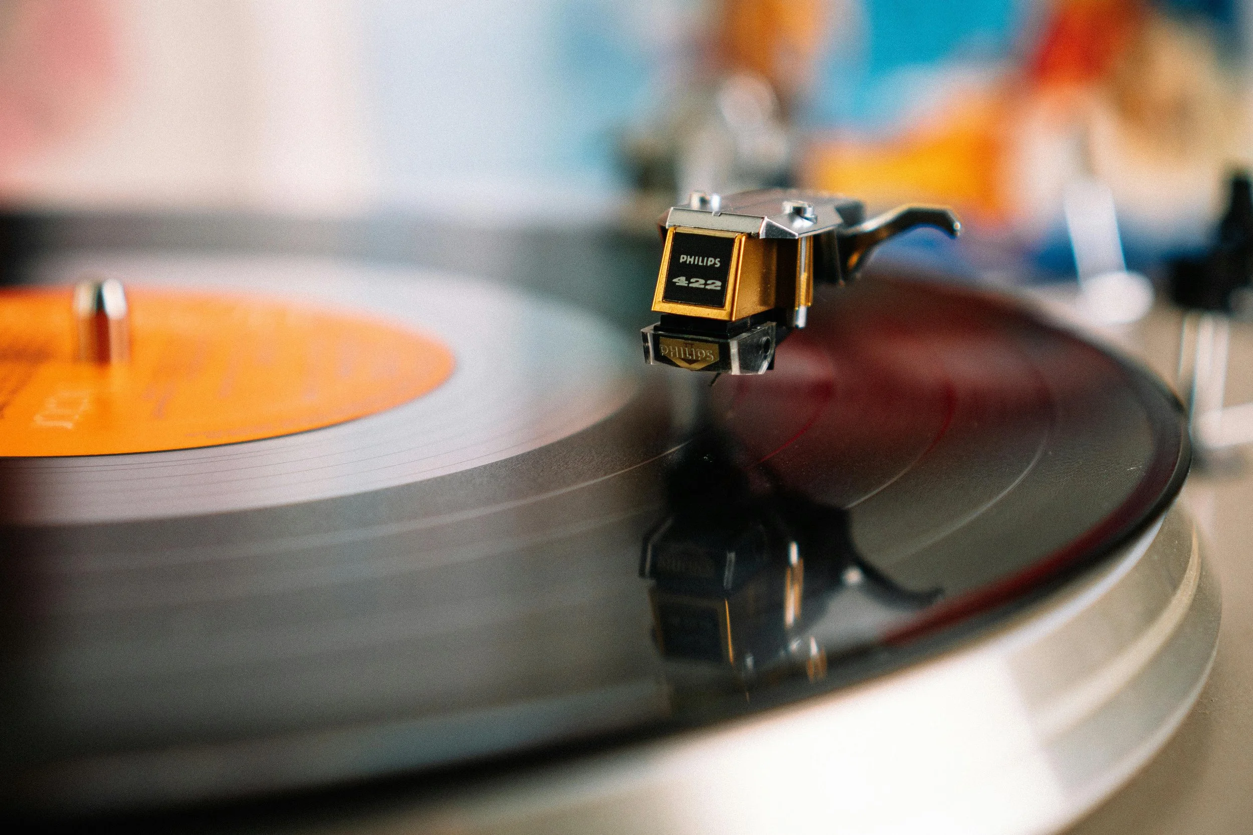 Close-up of a vintage turntable playing a vinyl record with a bright orange label.