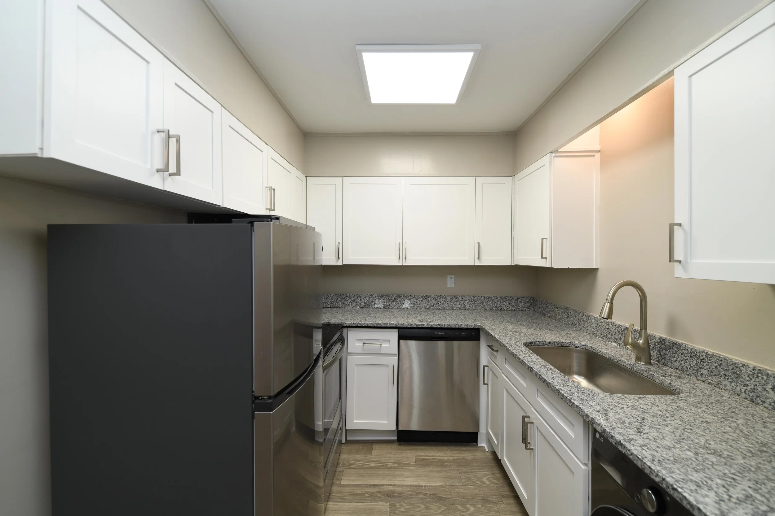 Kitchen with white cabinets, granite countertops, stainless steel appliances, a sink, and a ceiling light fixture.