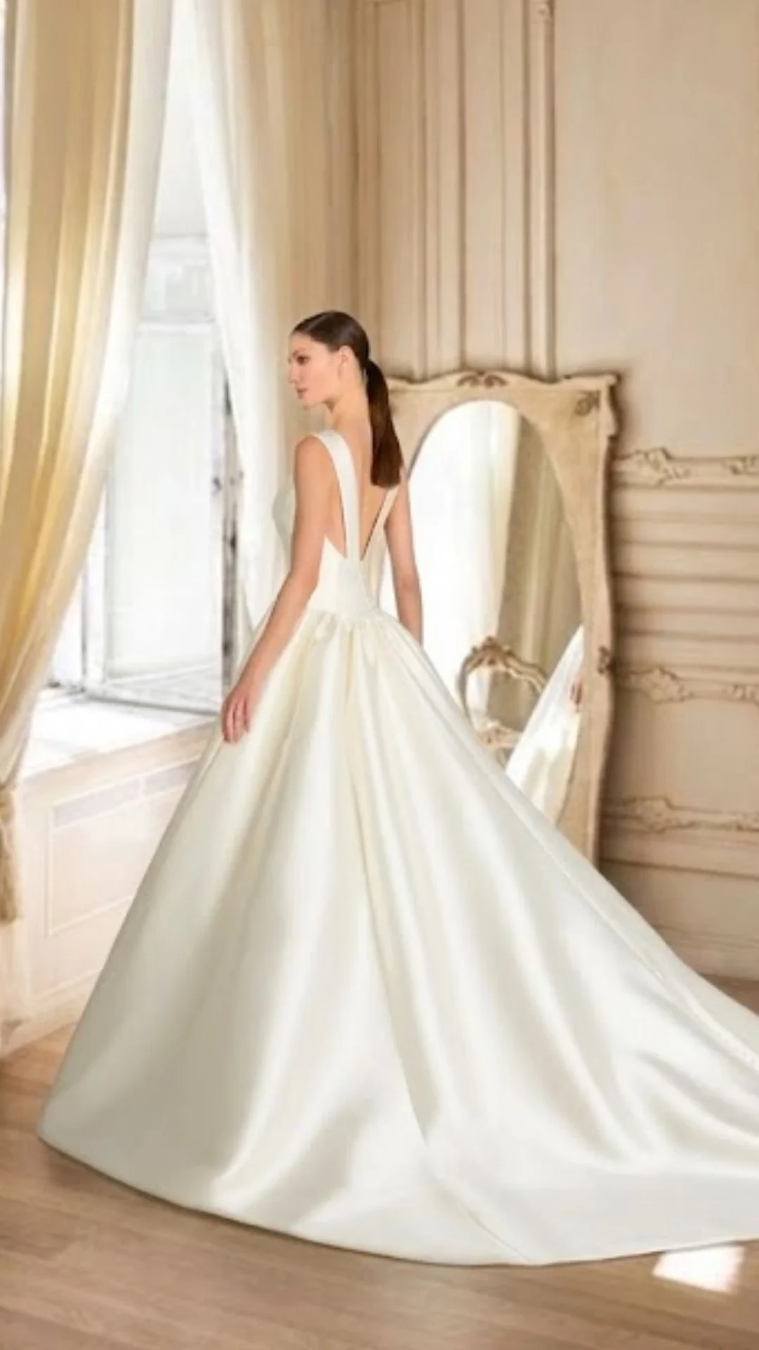 Mulher de vestido de noiva branco em um quarto com espelho antigo.