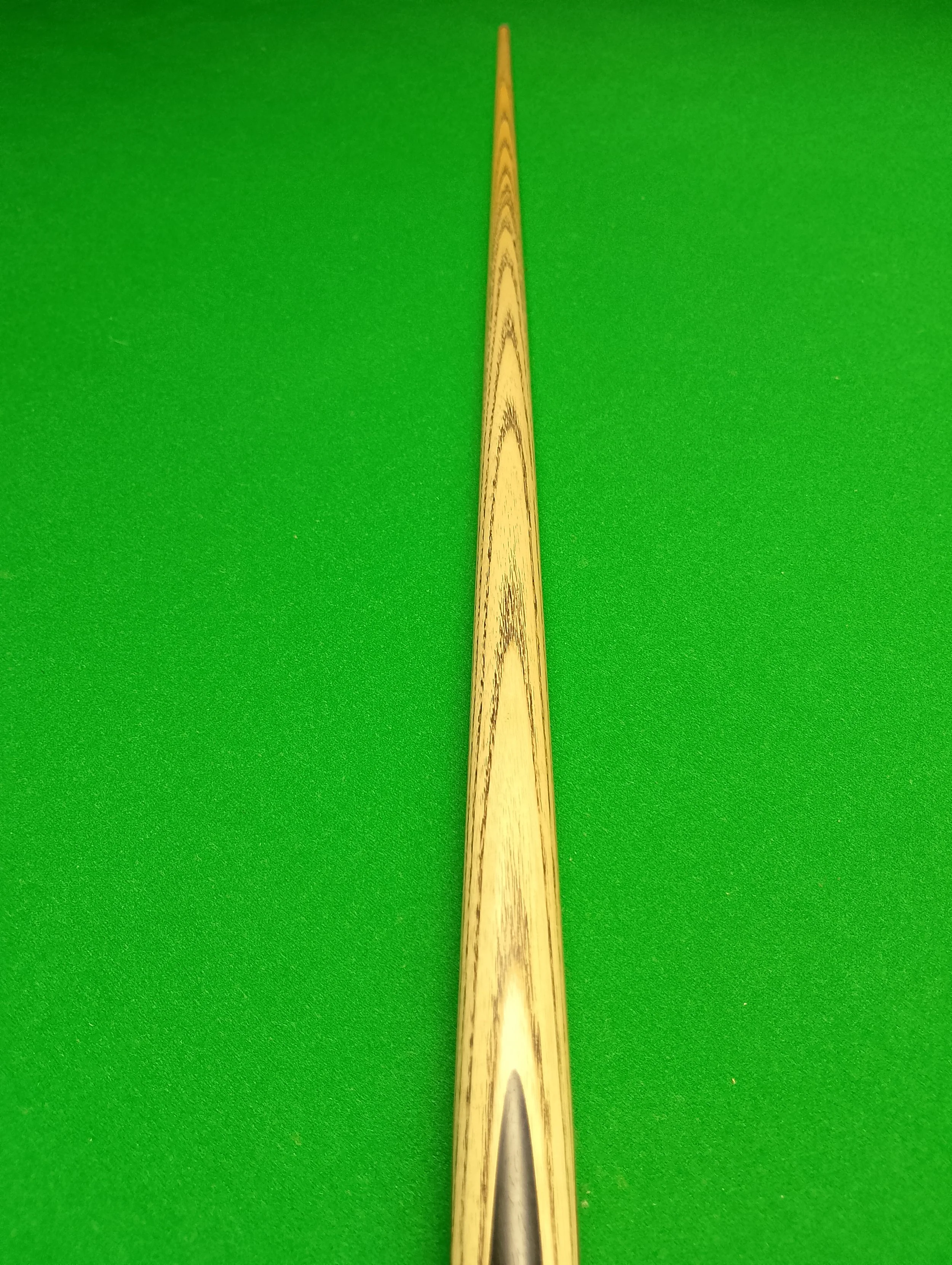 A close-up view of a pool cue stick on a green pool table surface.