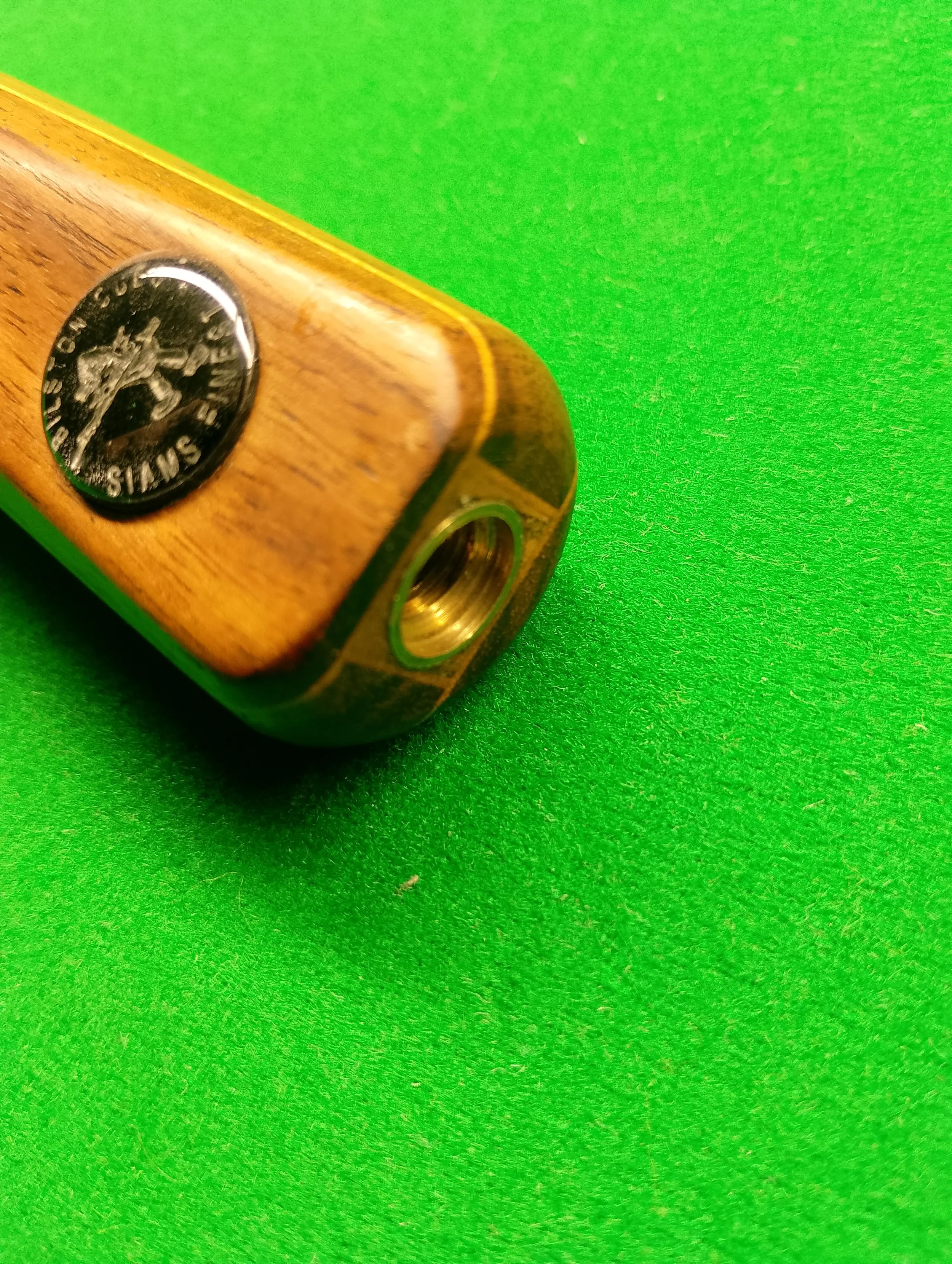 Close-up of a wooden pool cue with a silver emblem on a green felt surface.