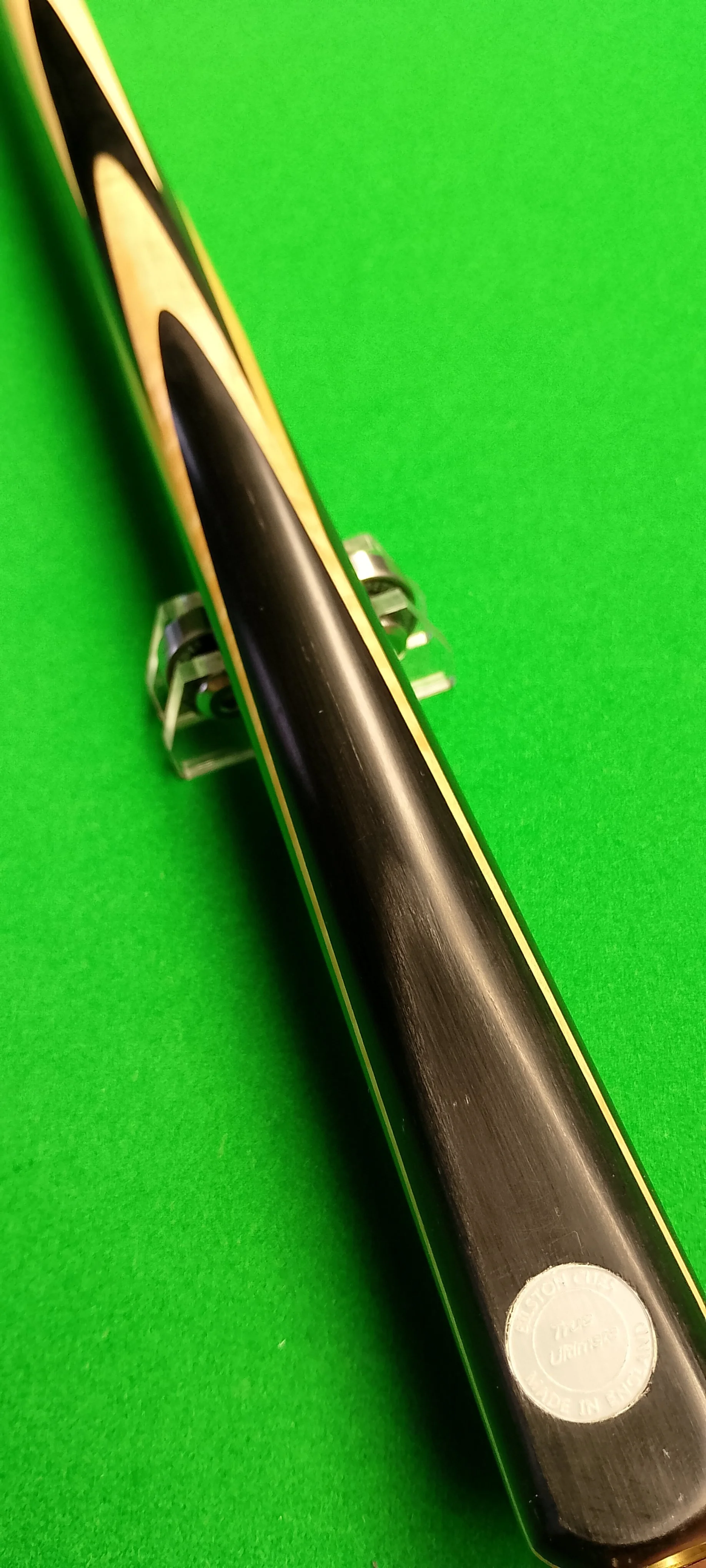 Top view of a pool cue with black and yellow design resting on clear plastic racks on a green pool table.
