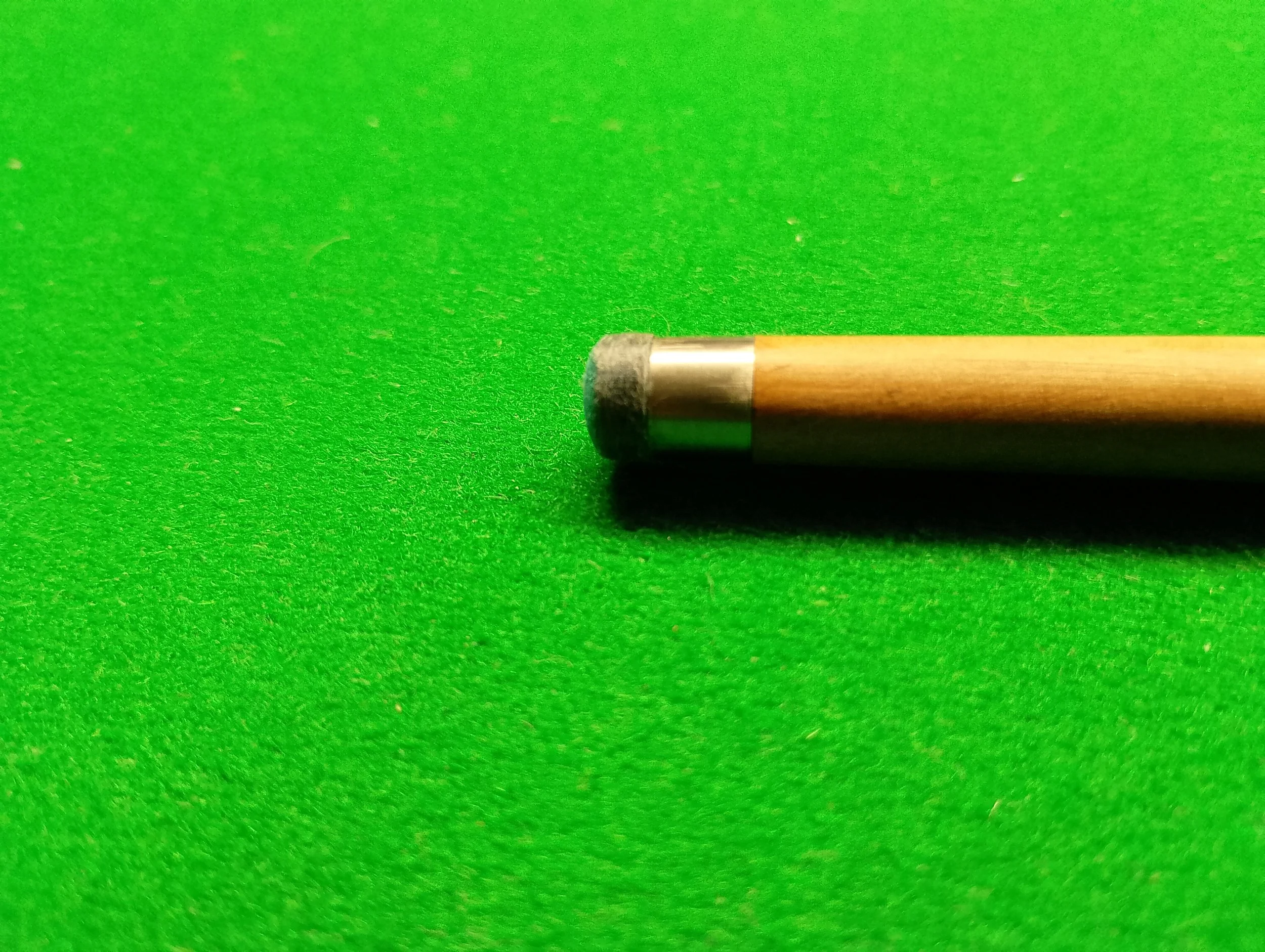 Close-up of a billiard cue stick with a black tip on a green felt pool table