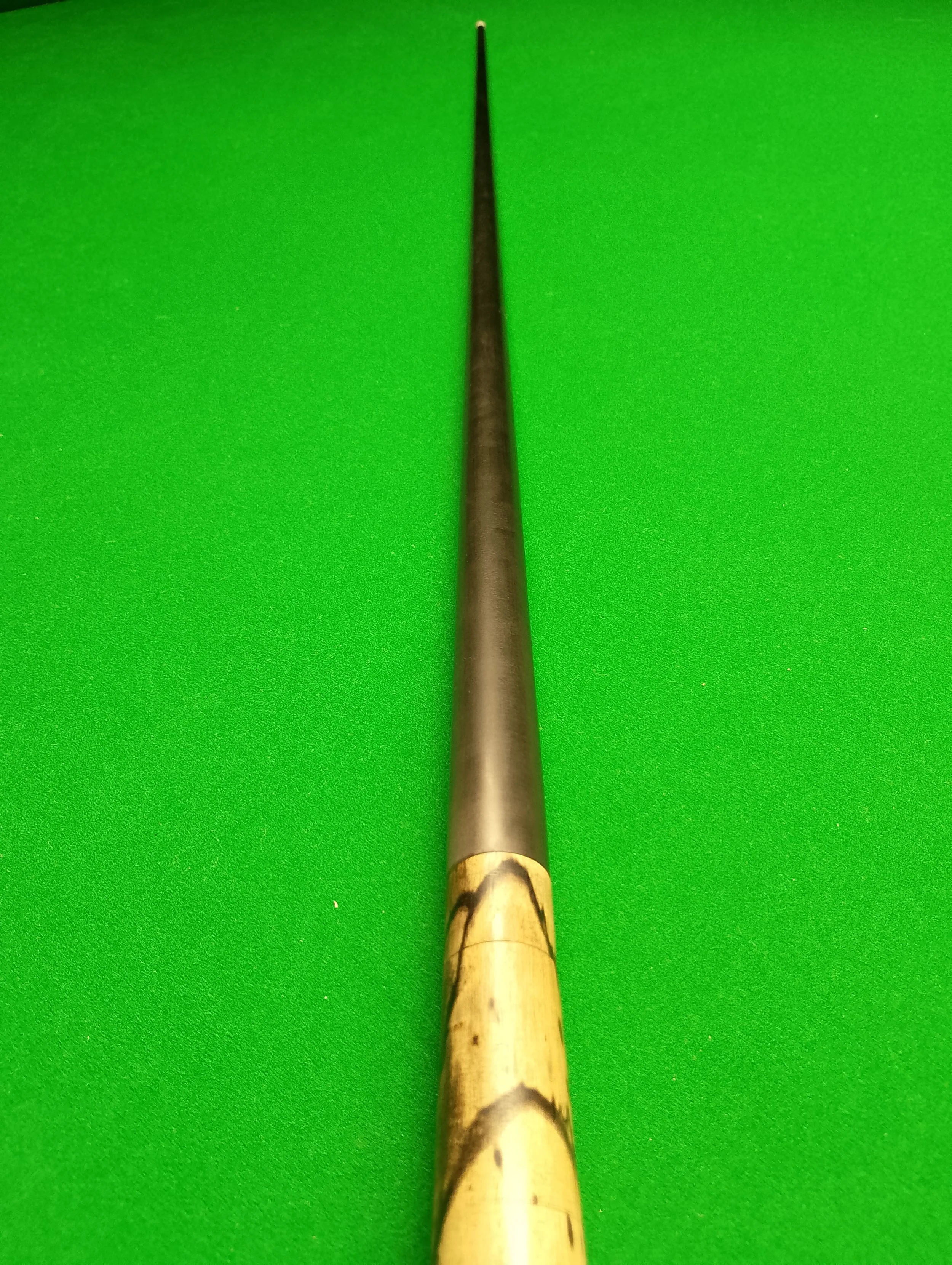 A cue stick with a bamboo handle lying on a green pool table.