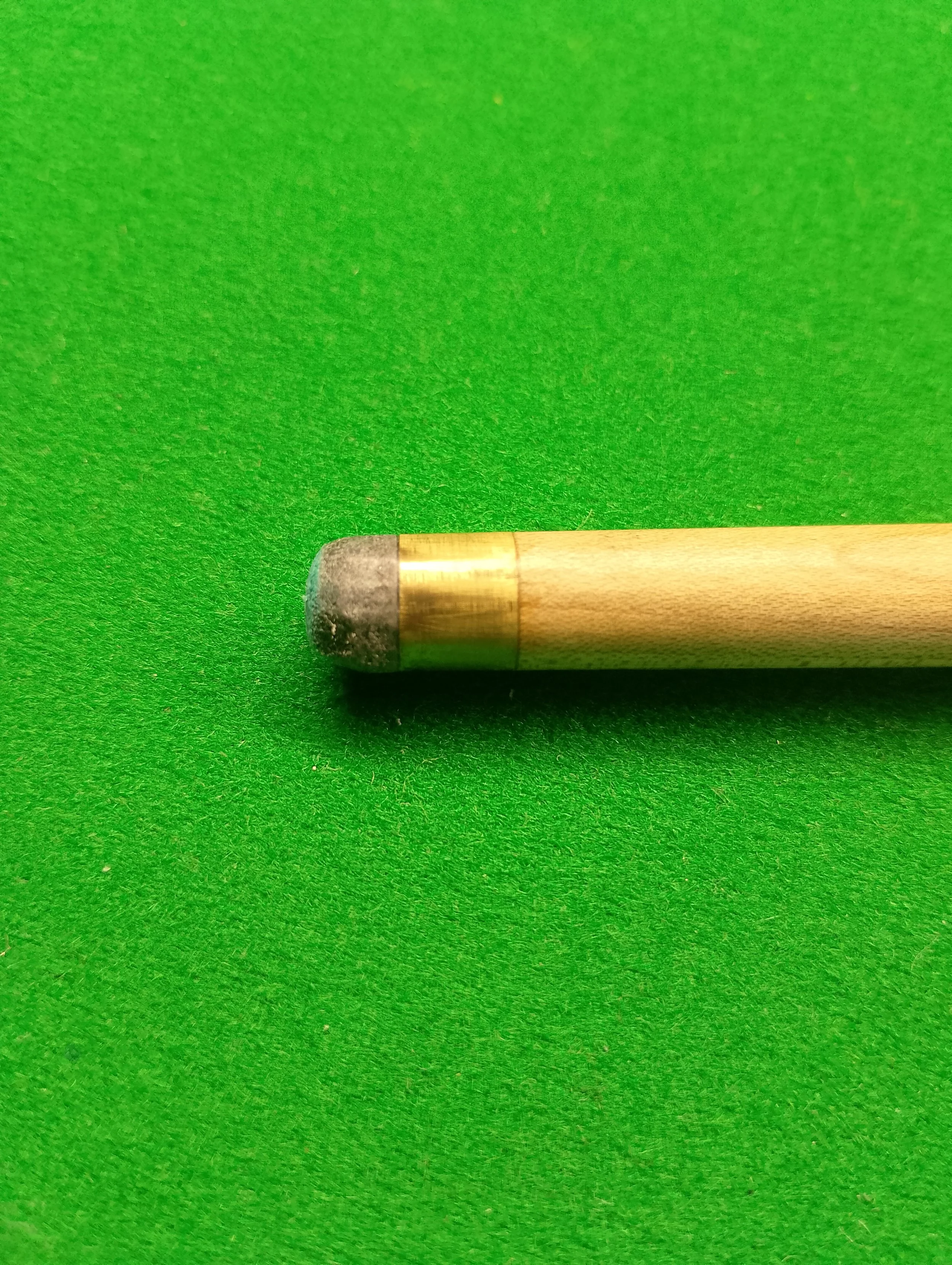 Close-up of a wooden cue stick with chalked tip on a green billiard table.