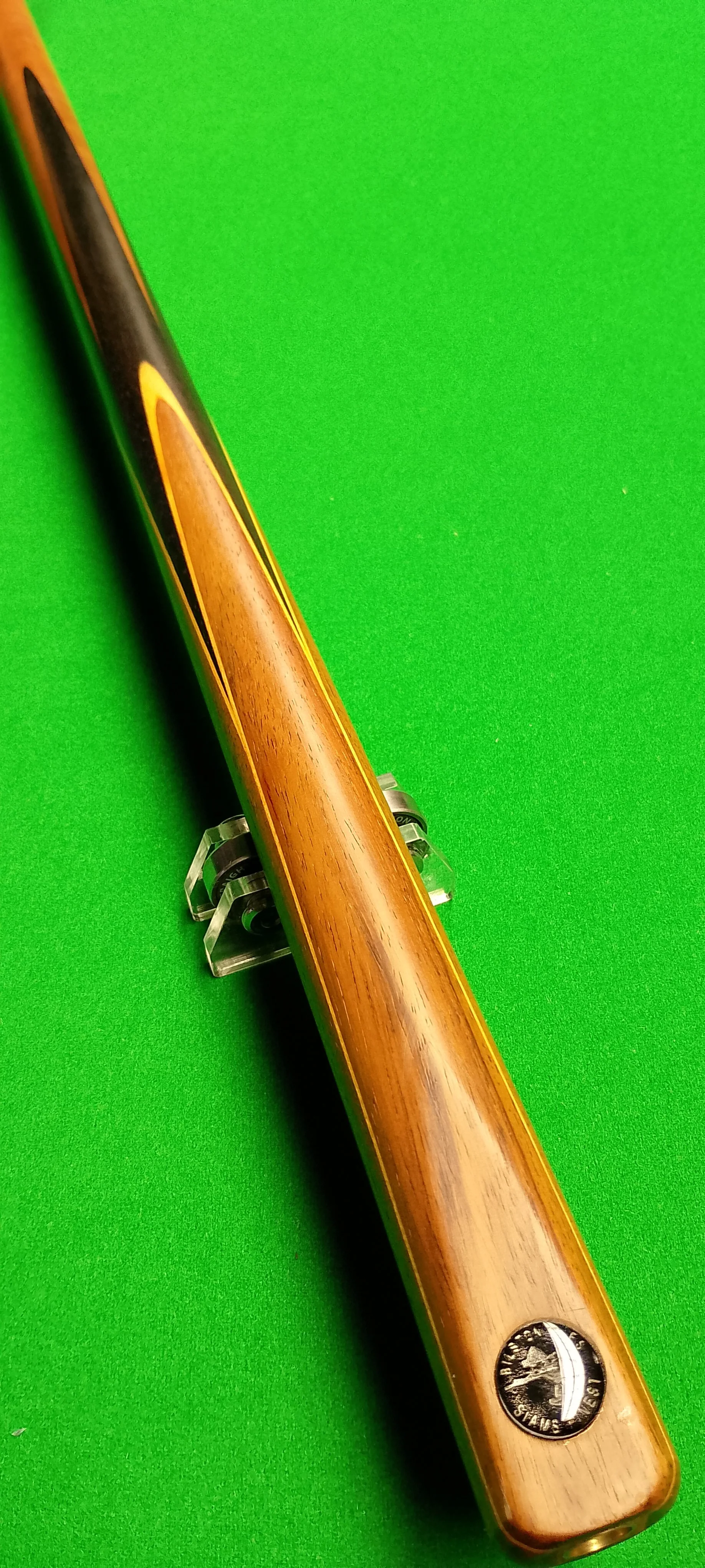 Close-up of a wooden cue stick resting on a green pool table with a transparent cue stand.
