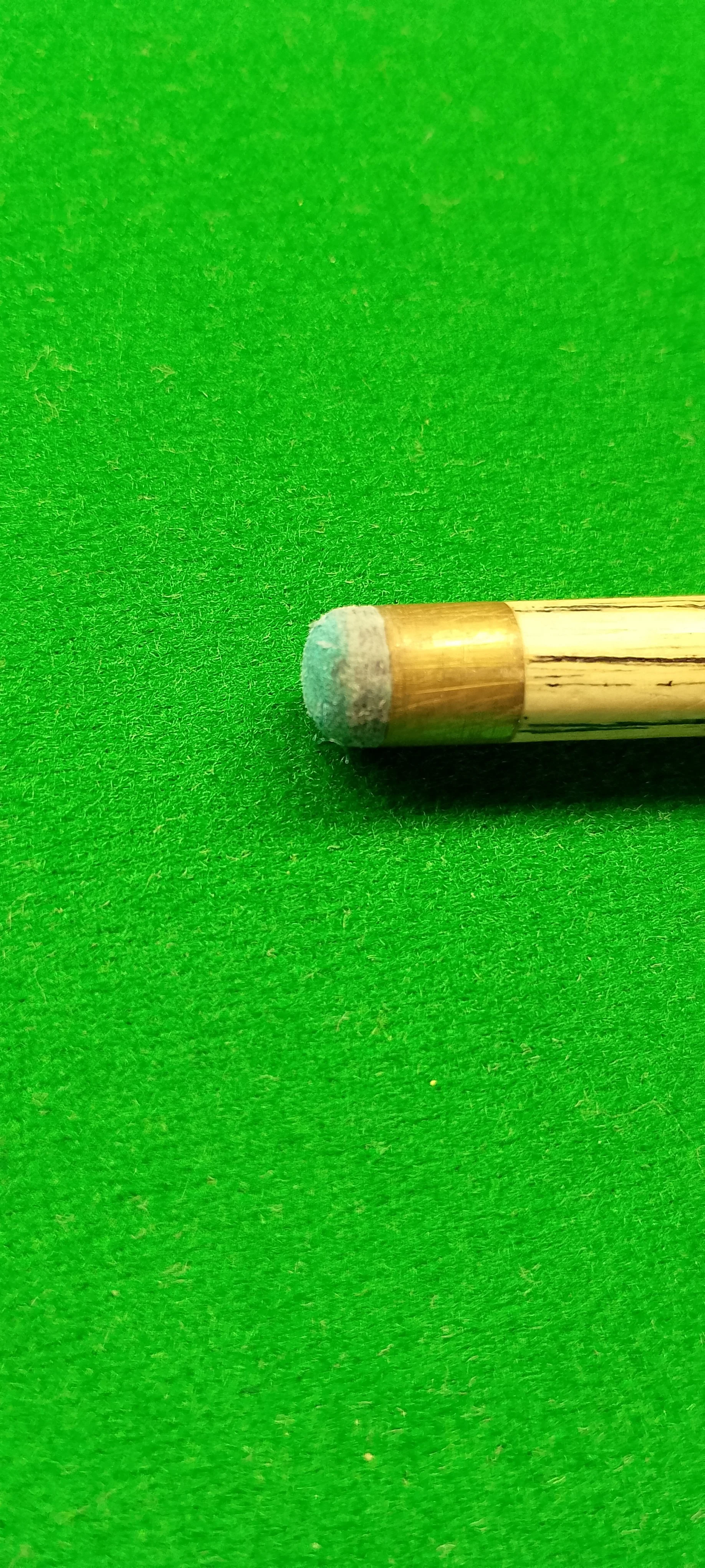 Close-up of a billiard cue tip on a green pool table.