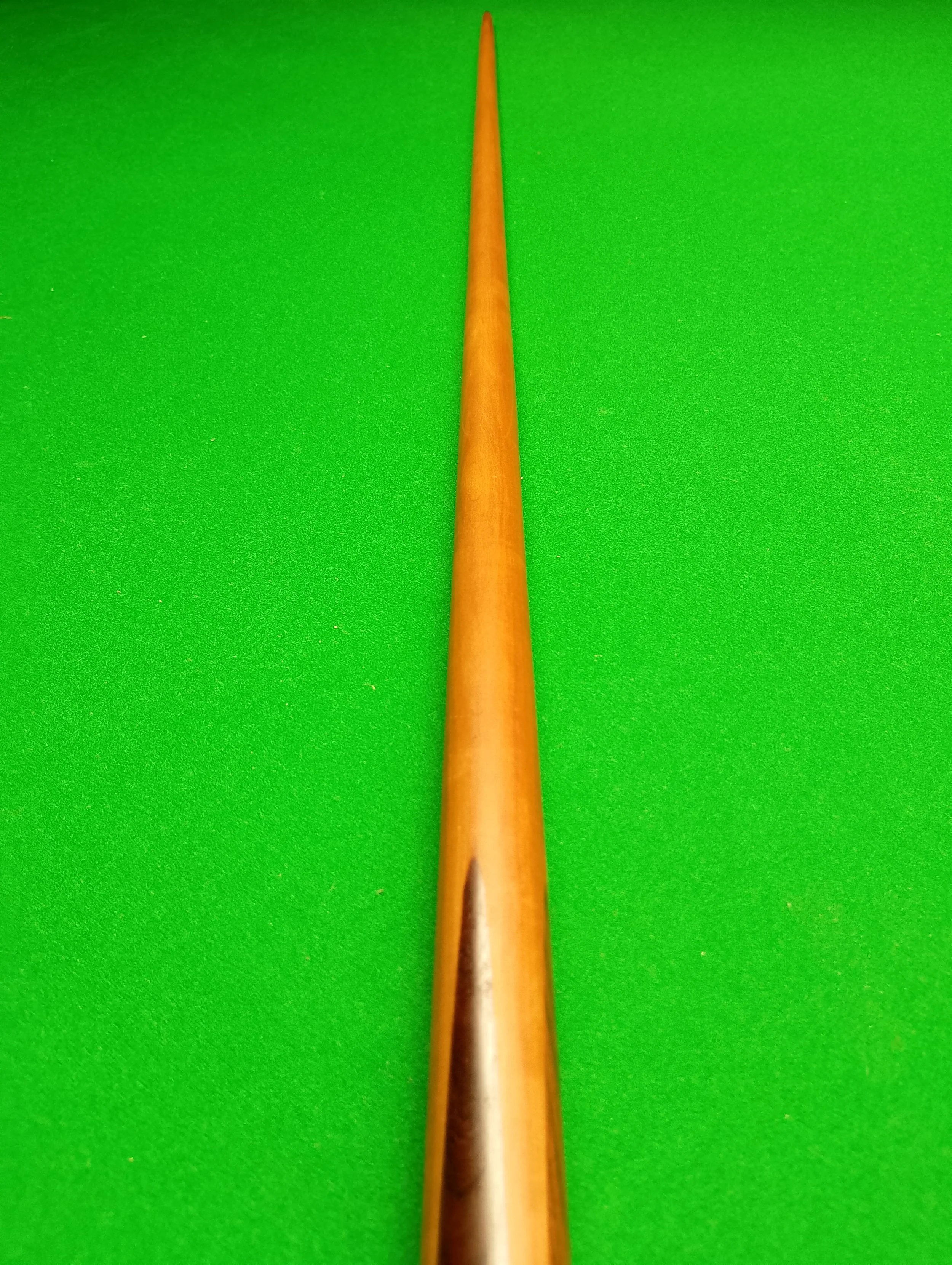 A snooker cue stick placed on a green felt table, viewed from its tip to the butt.
