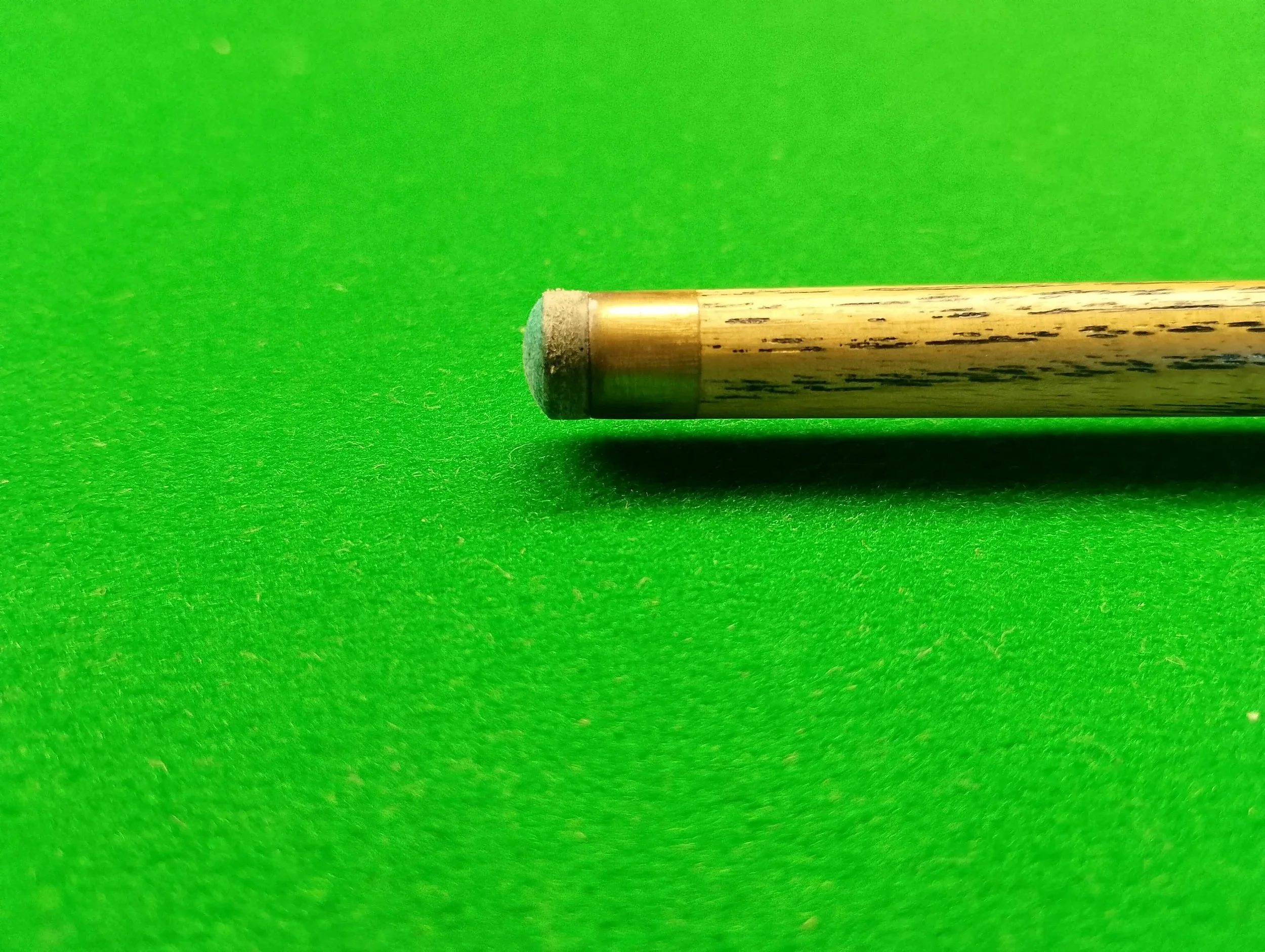 Close-up of a pool cue resting on a green pool table surface.