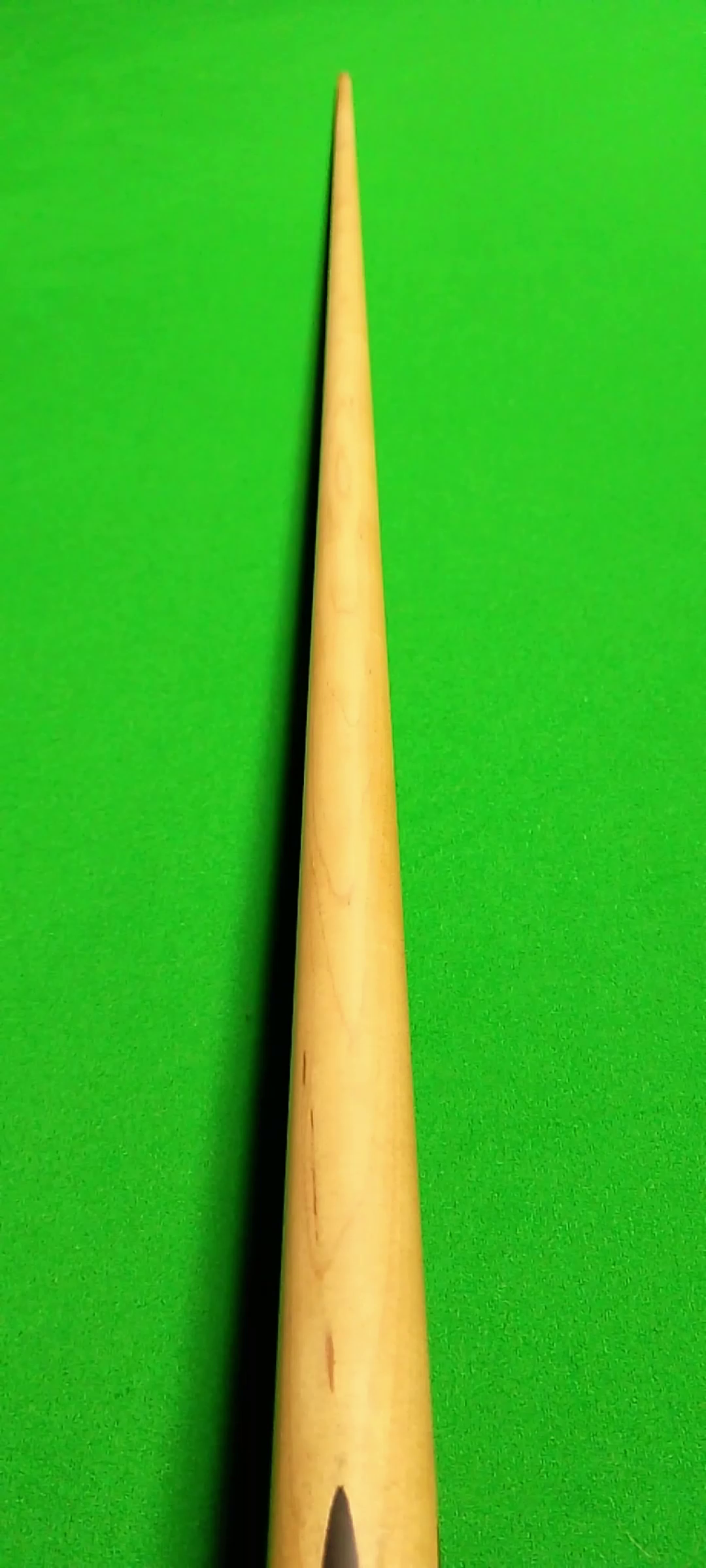 Close-up of a wooden stick or cue stick against a bright green background.