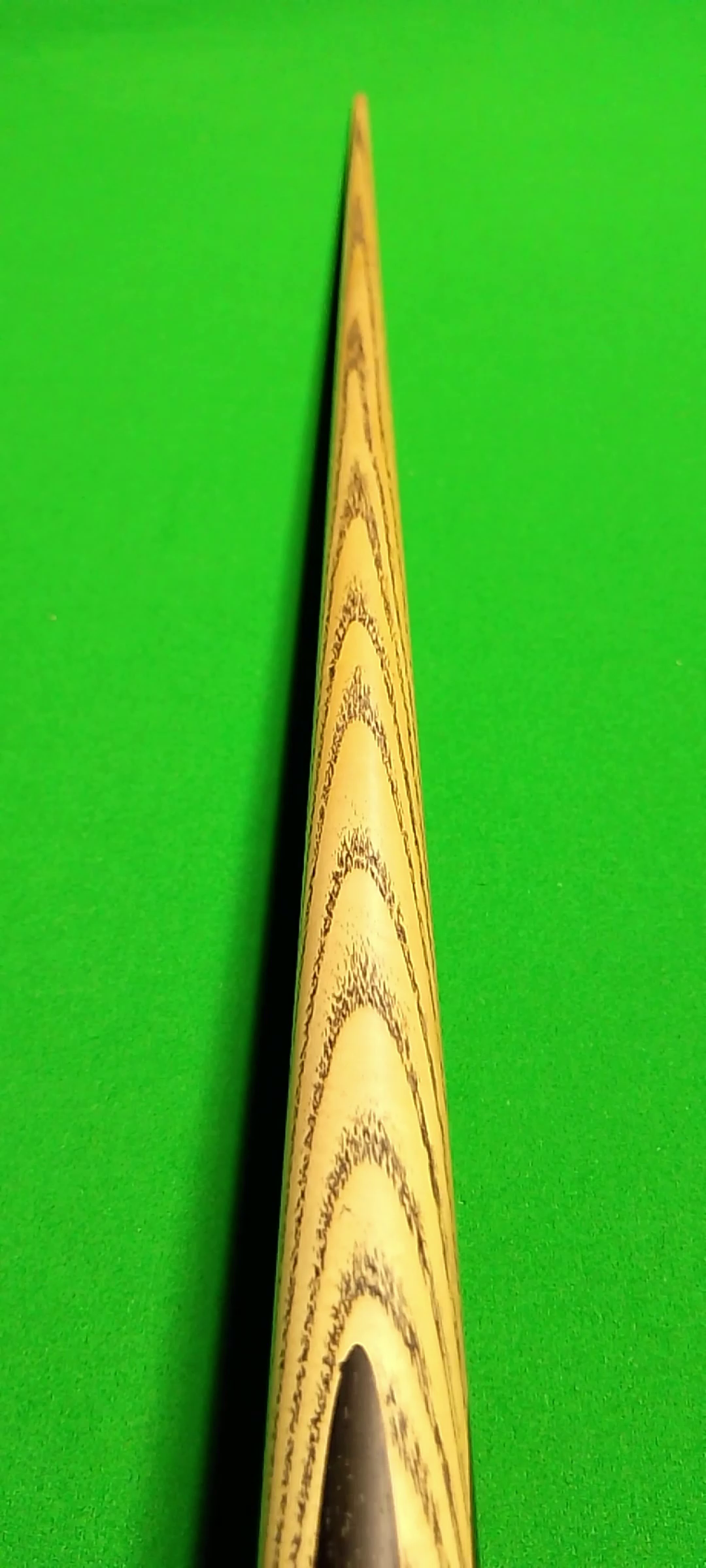 Close-up of a wooden billiard cue stick on a green billiard table.