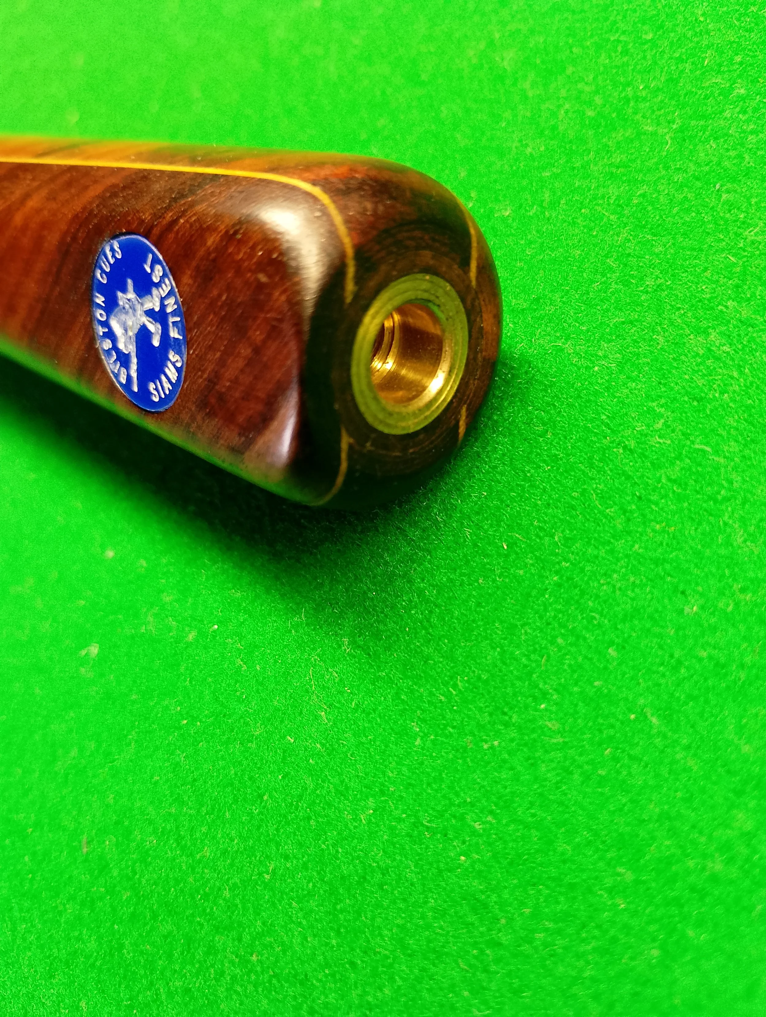 Close-up of a wood billiard cue with a brass joint on a green felt table.