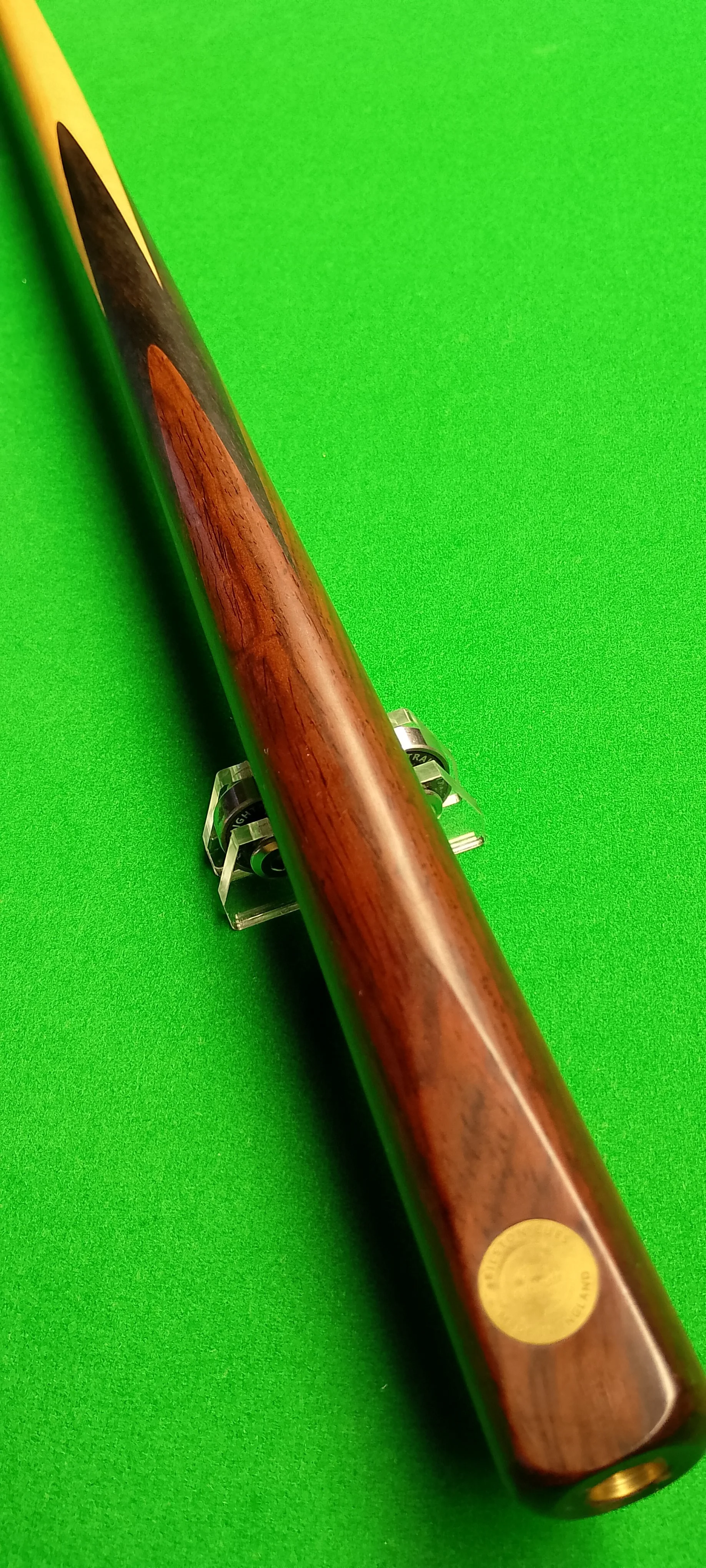 A wooden billiard cue stick with a black tip, placed on a green pool table surface.