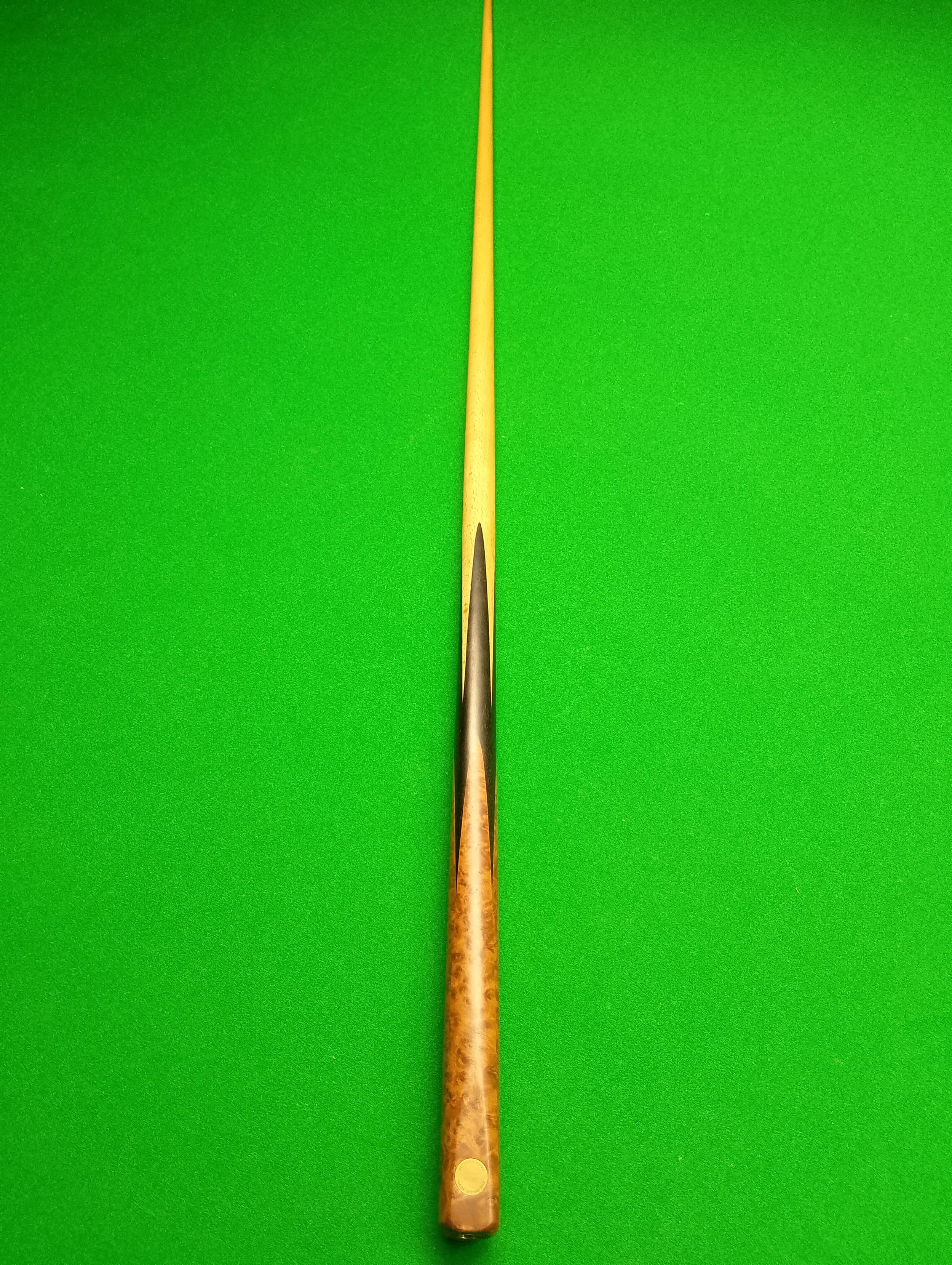 A wooden cue stick placed vertically on a green pool table.