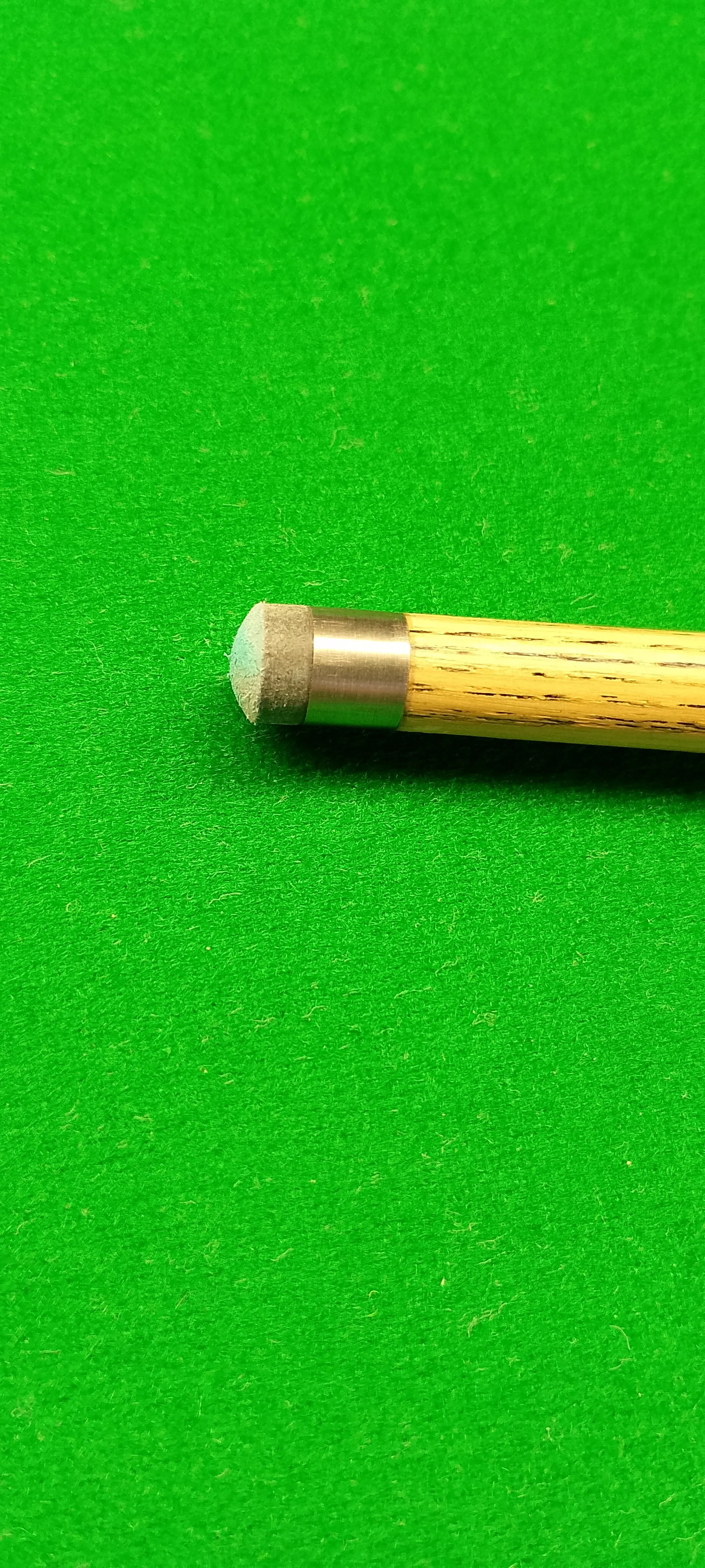 Close-up of a cue tip on a billiards cue stick resting on a green felt surface.