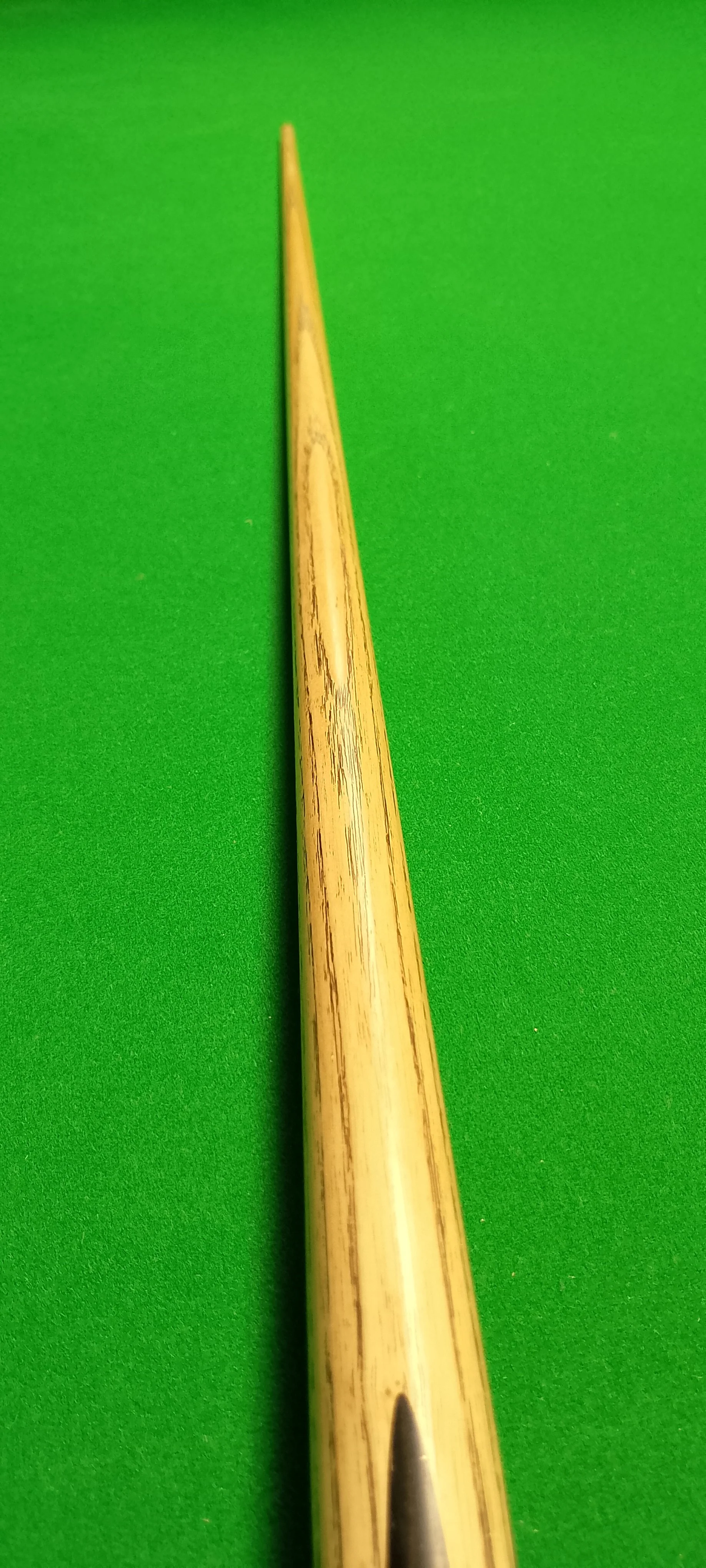 Close-up of a wooden pool cue on a green pool table.