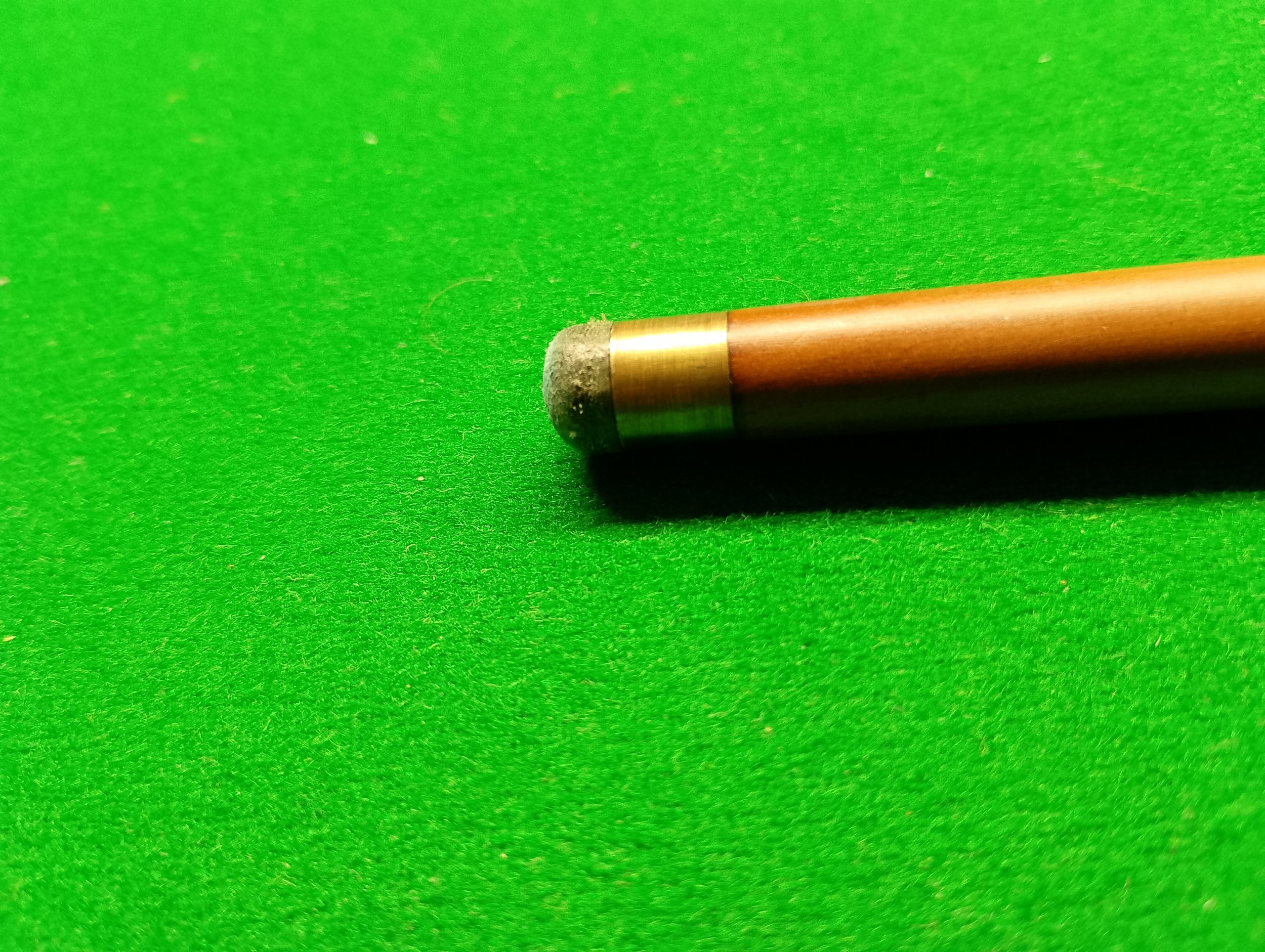 Close-up of a cue stick tip on a green pool table surface.