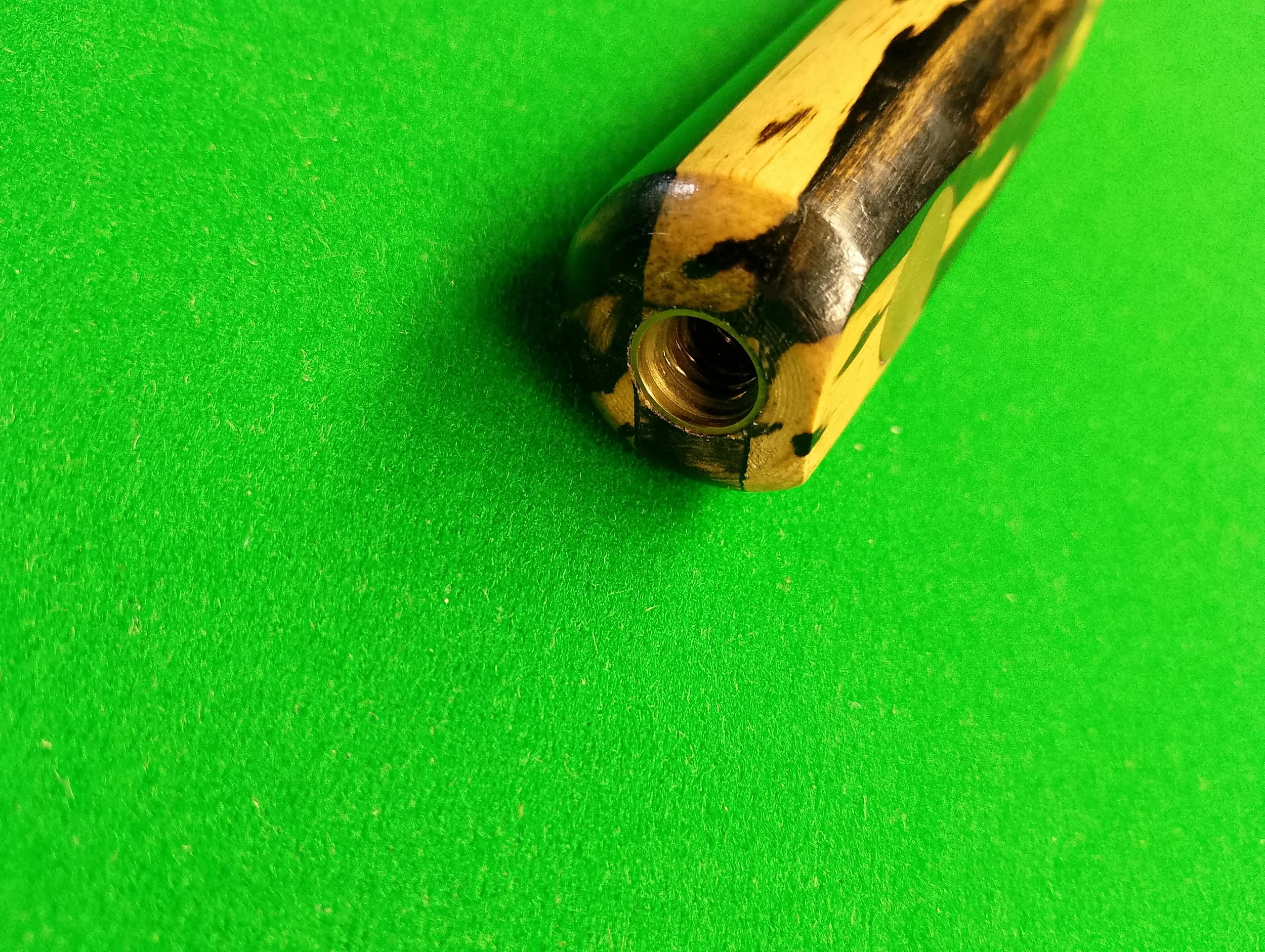 The image shows a yellow and black patterned object, likely a vape or a similar device, placed on a green textured surface. The device is positioned at an angle, showing its open mouthpiece or connection point.