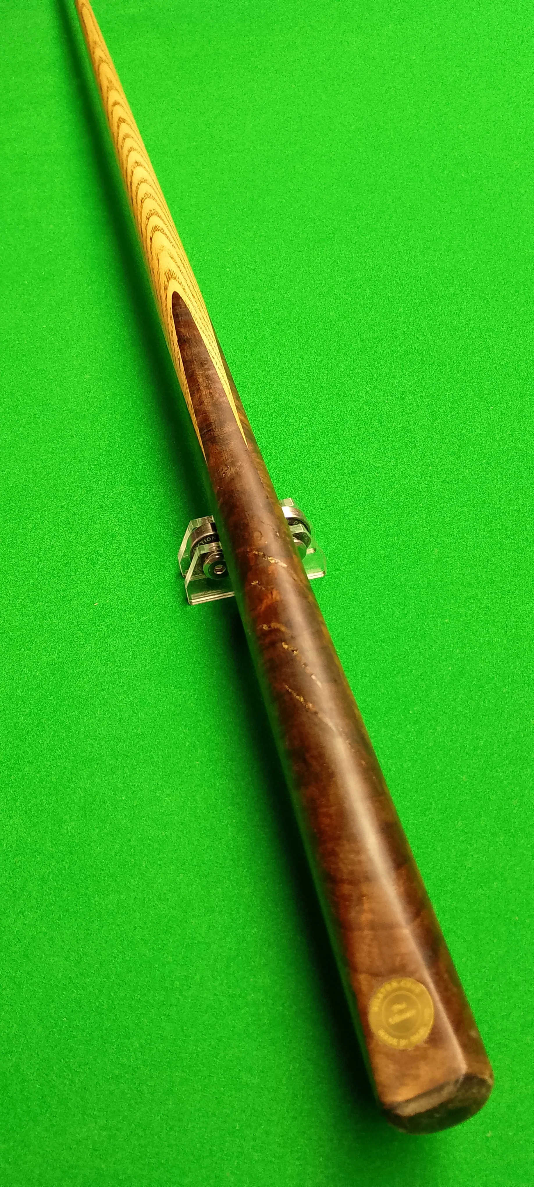 A pool cue with a wooden handle resting on a green pool table surface.