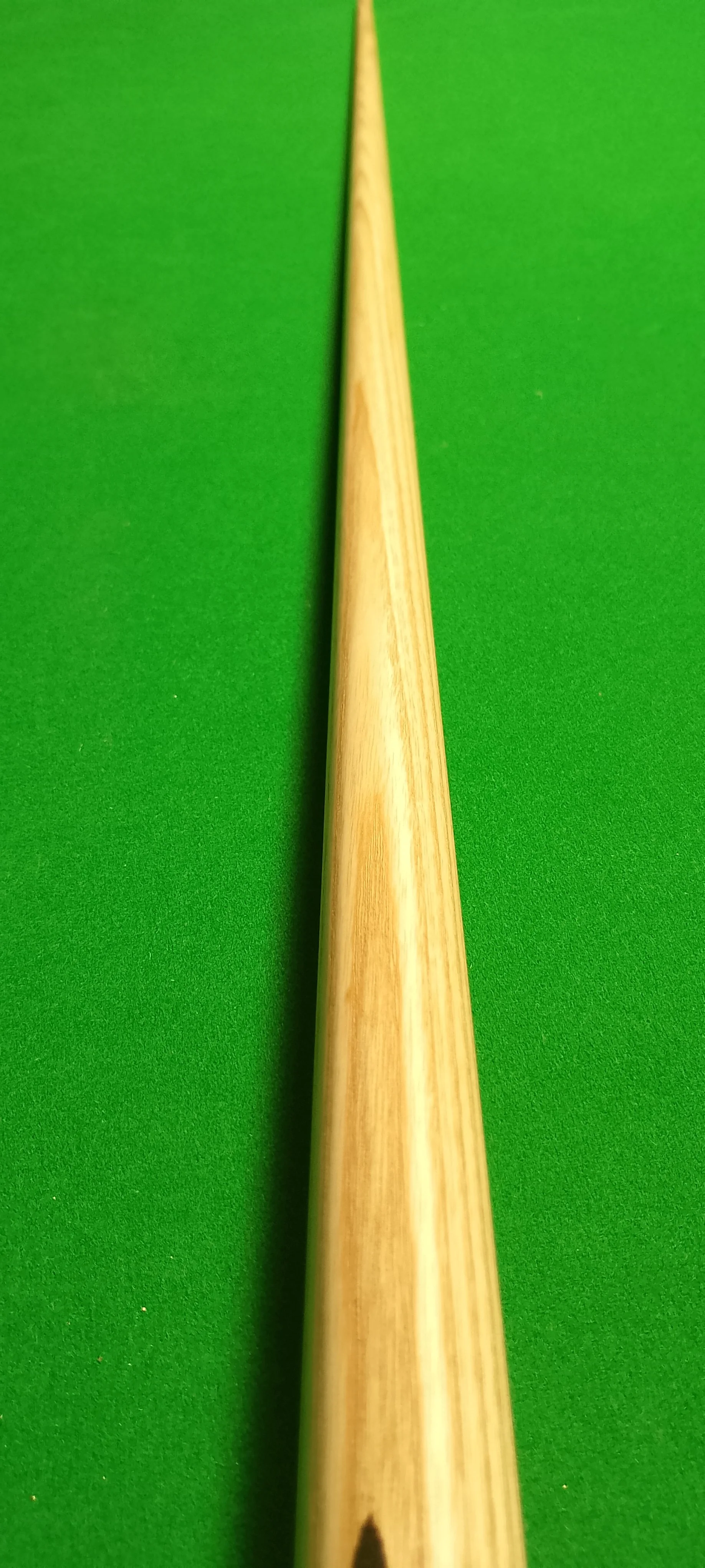 Close-up of a wooden cue stick on a green pool table felt.