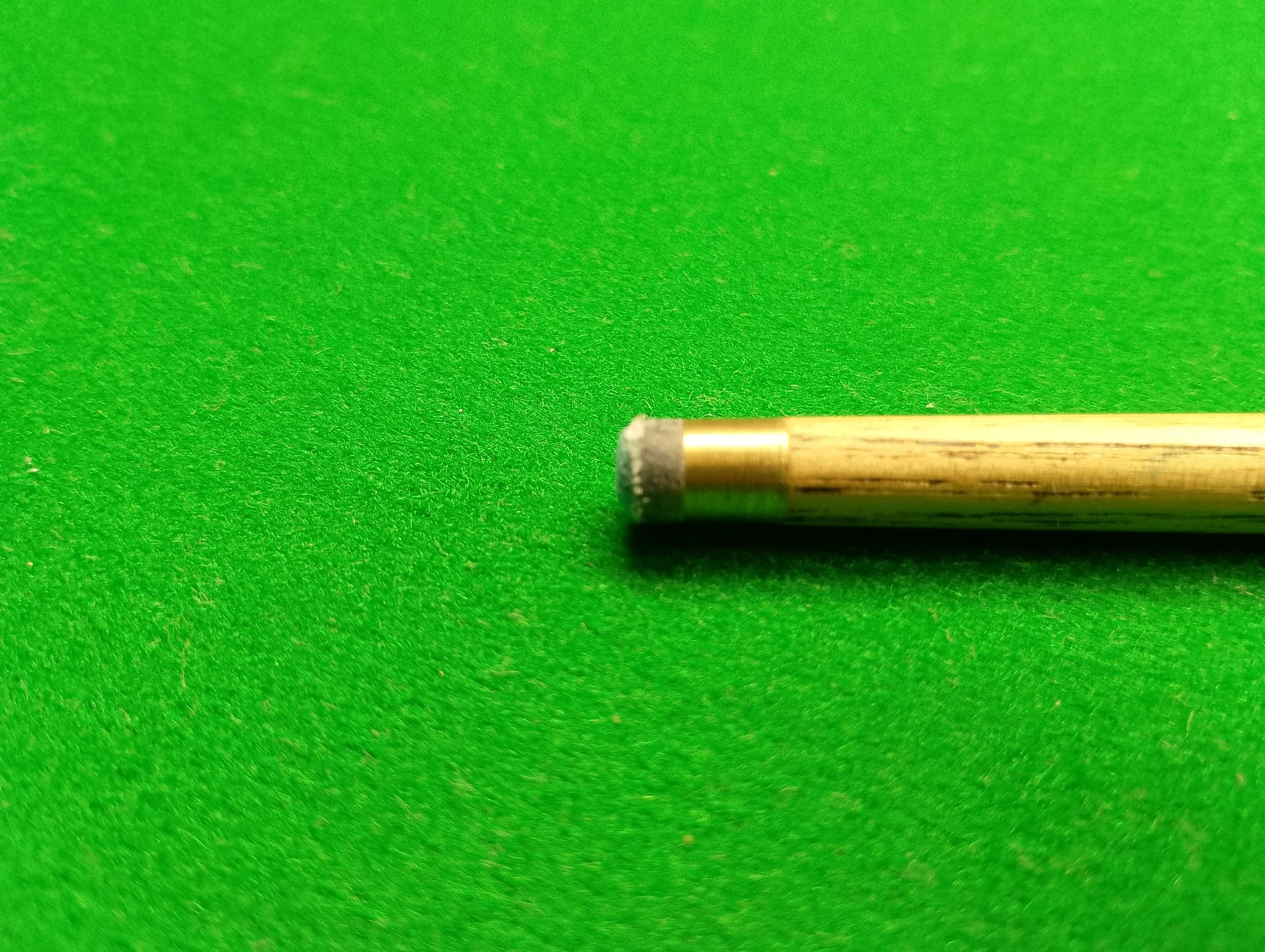 Close-up of a cue stick tip on green pool table felt.