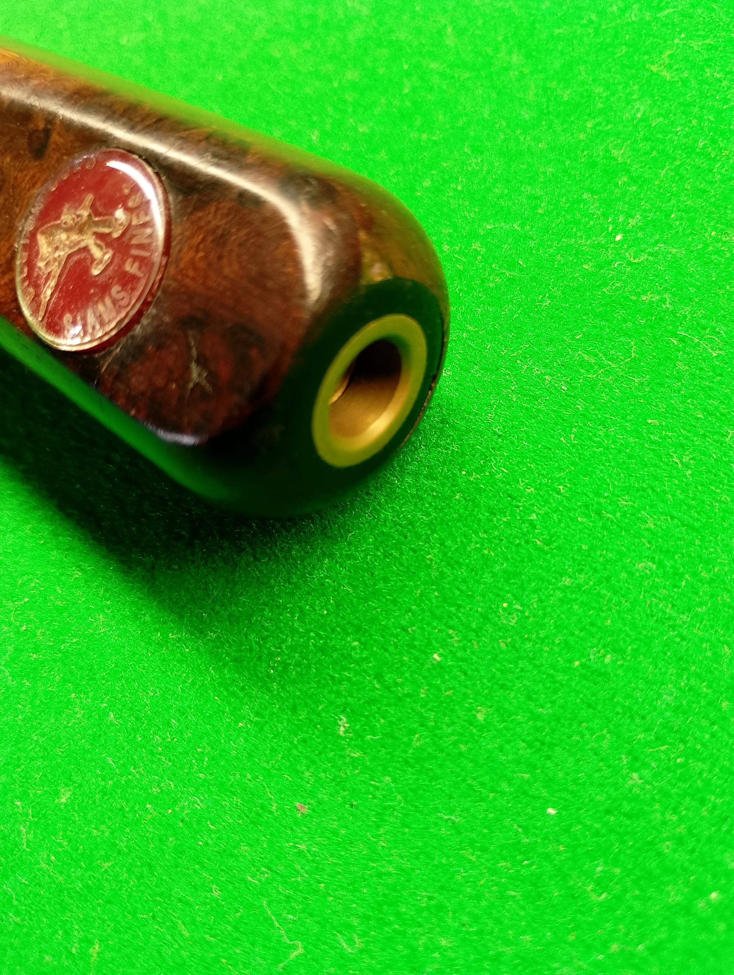 Close-up of a vintage brass and wood smoking pipe with a red logo on a green textured surface.