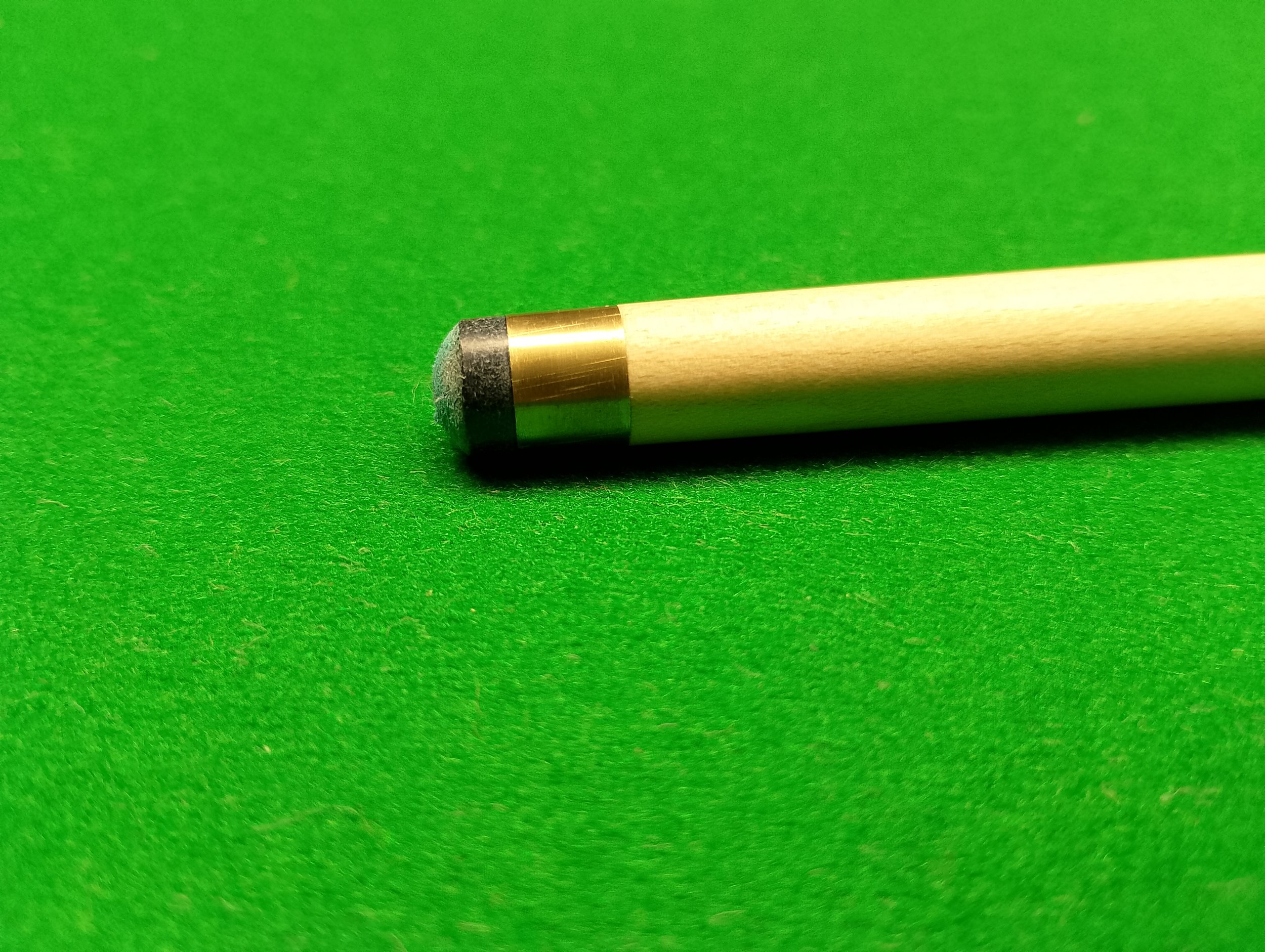 Close-up of a cue stick with black tip resting on a green pool table felt.