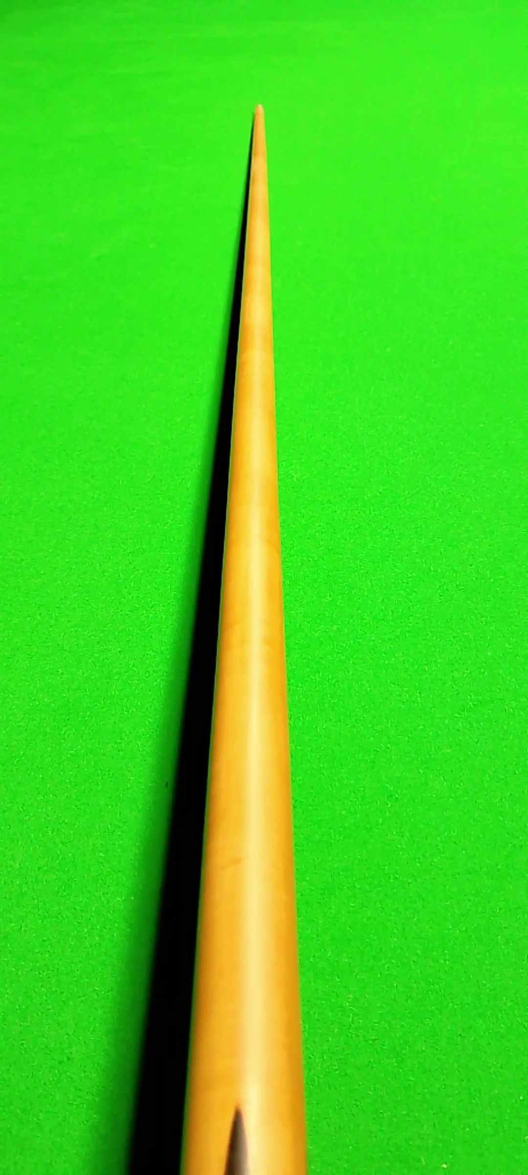 Close-up view of a yellow snooker cue on a bright green felt snooker table, viewed from close to the cue tip
