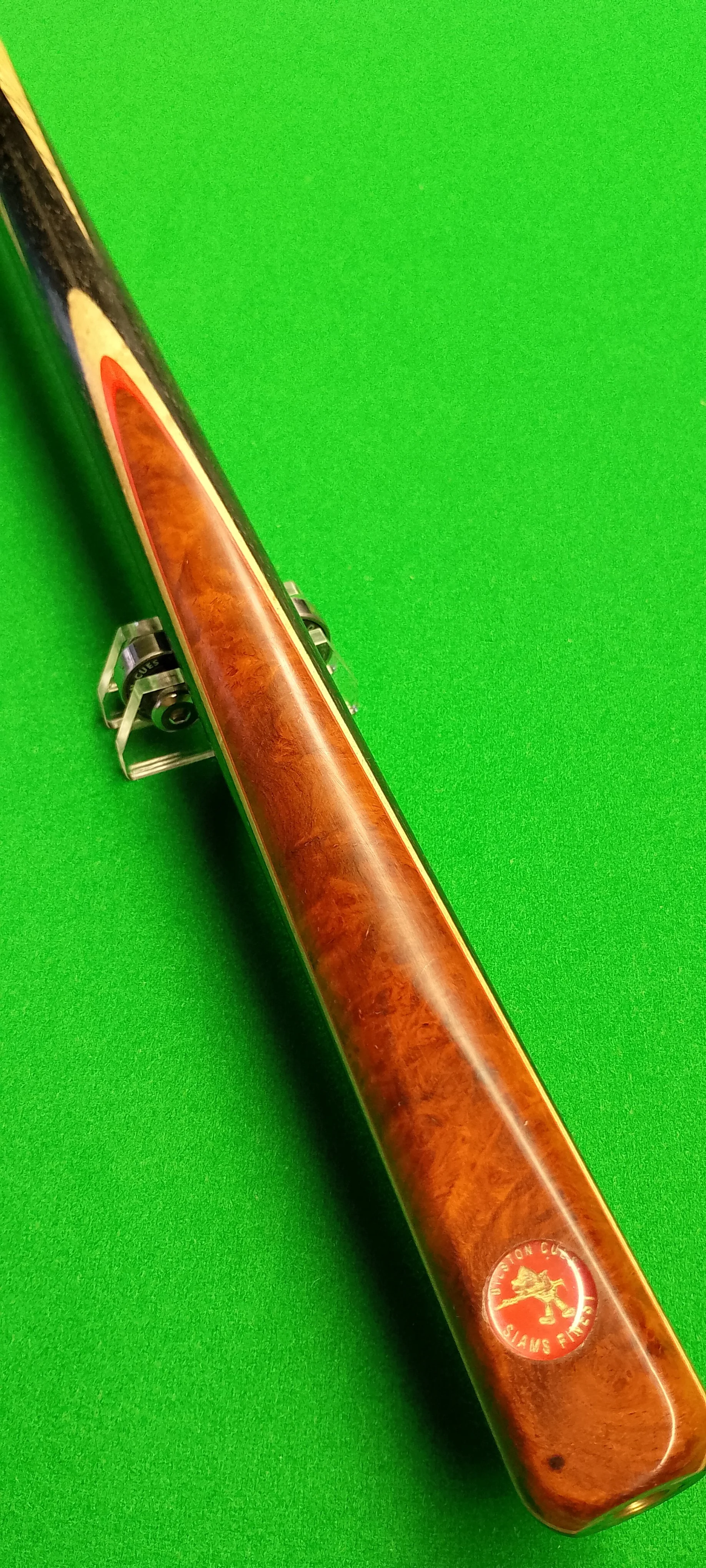Close-up of a pool cue with a wooden finish, resting on a green pool table with a cue stand.