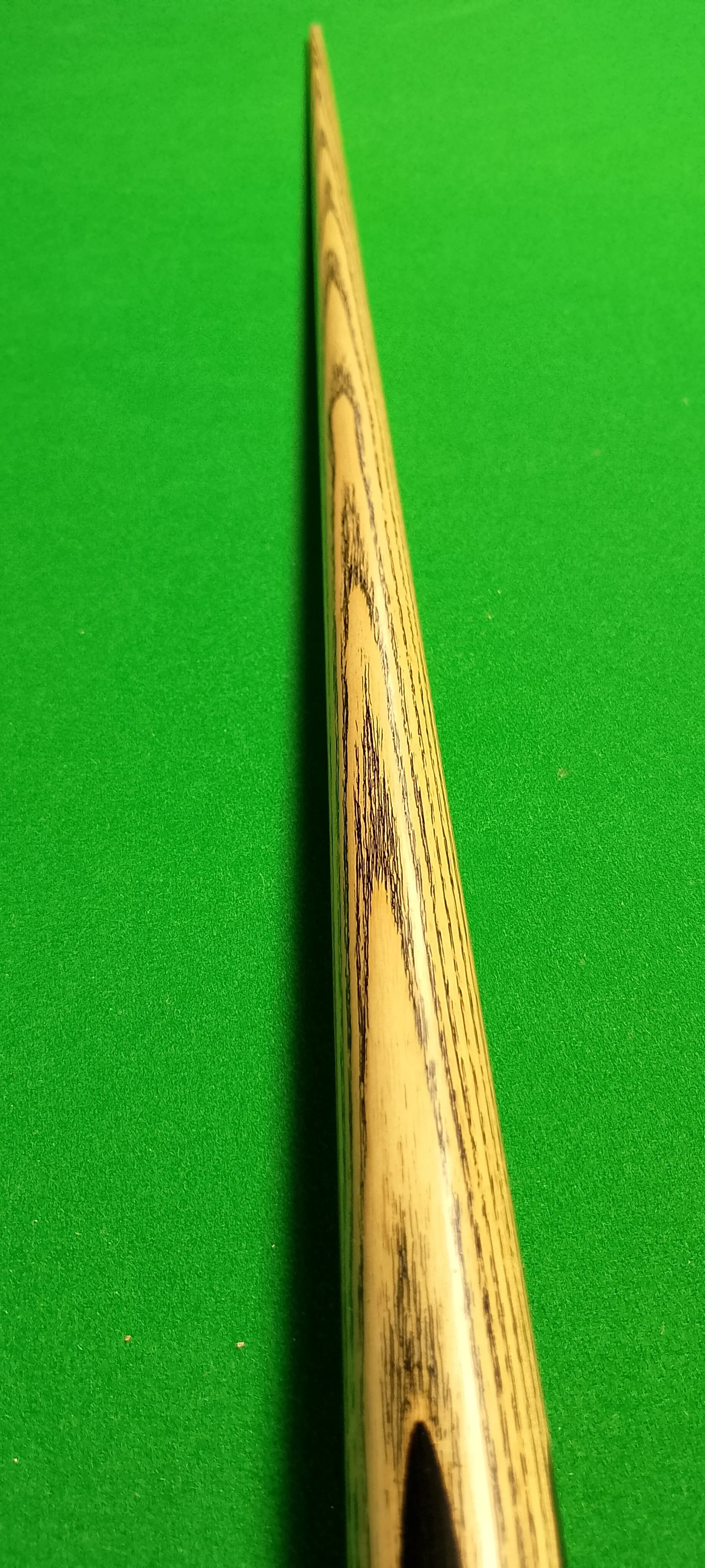 Close-up of a wooden pool cue stick on a green felt pool table.