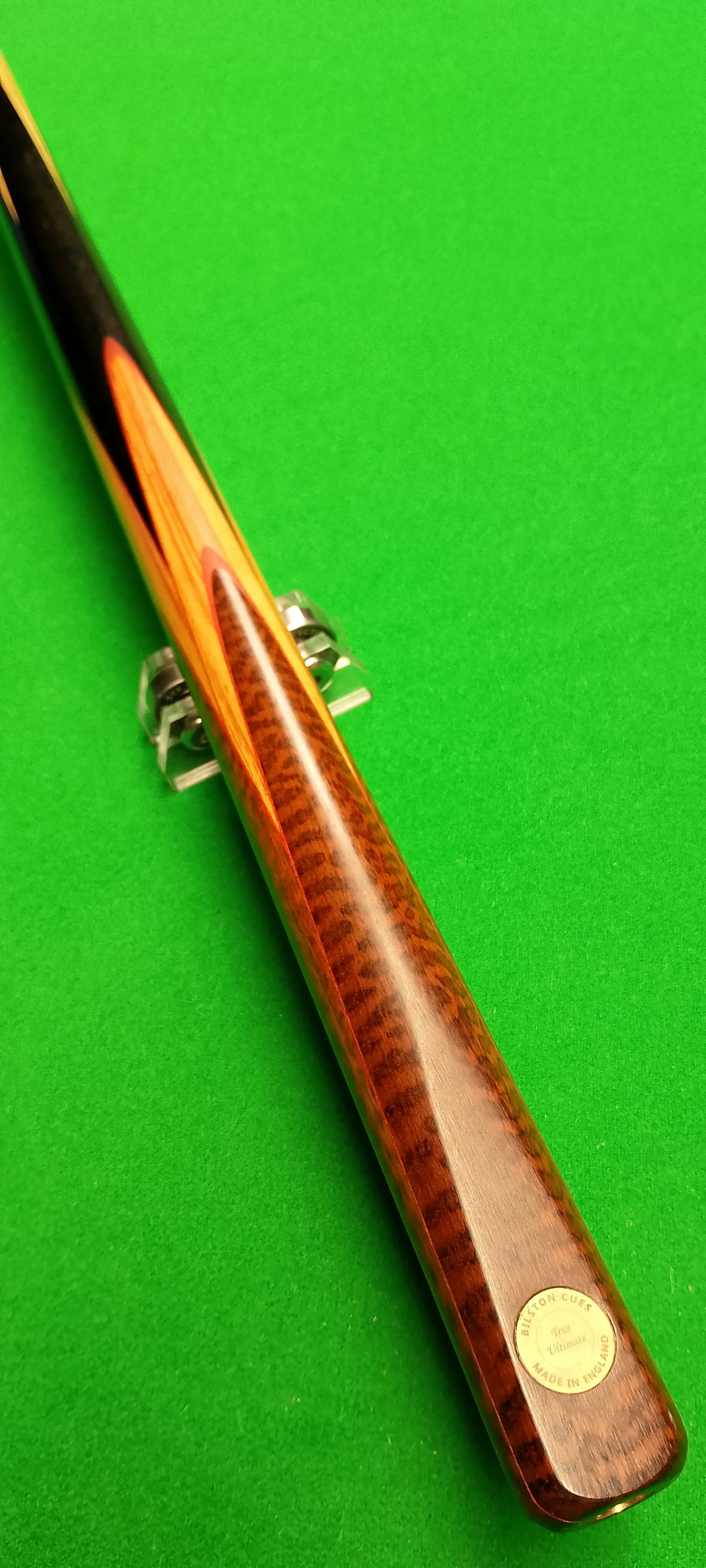 A billiard cue stick with a wooden finish resting on a green pool table felt.