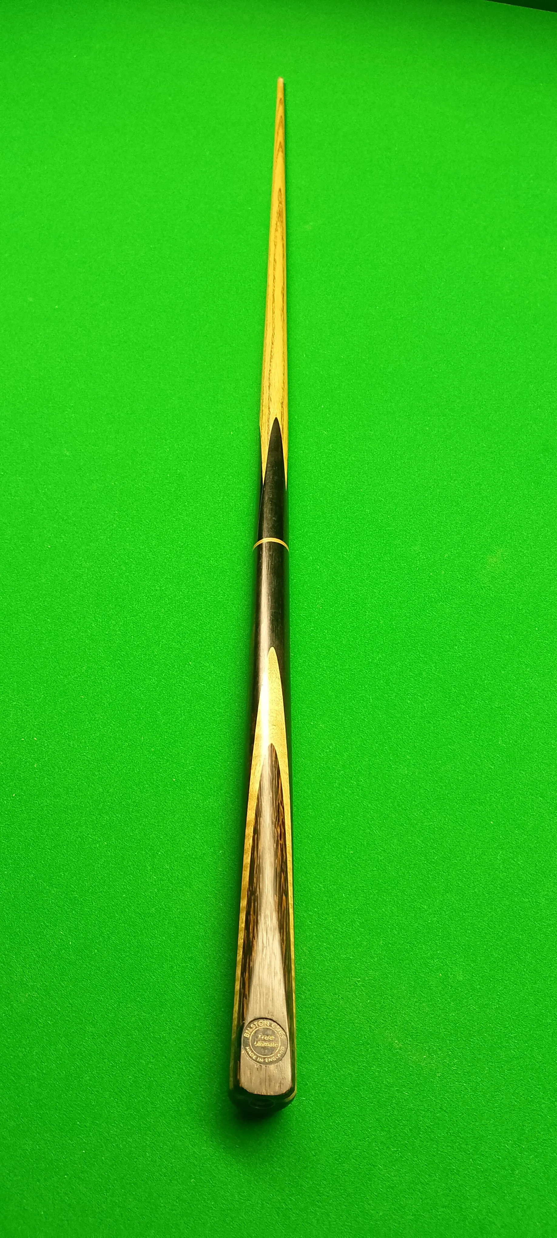 A pool cue stick with a black and wood pattern, laid flat on a bright green pool table.