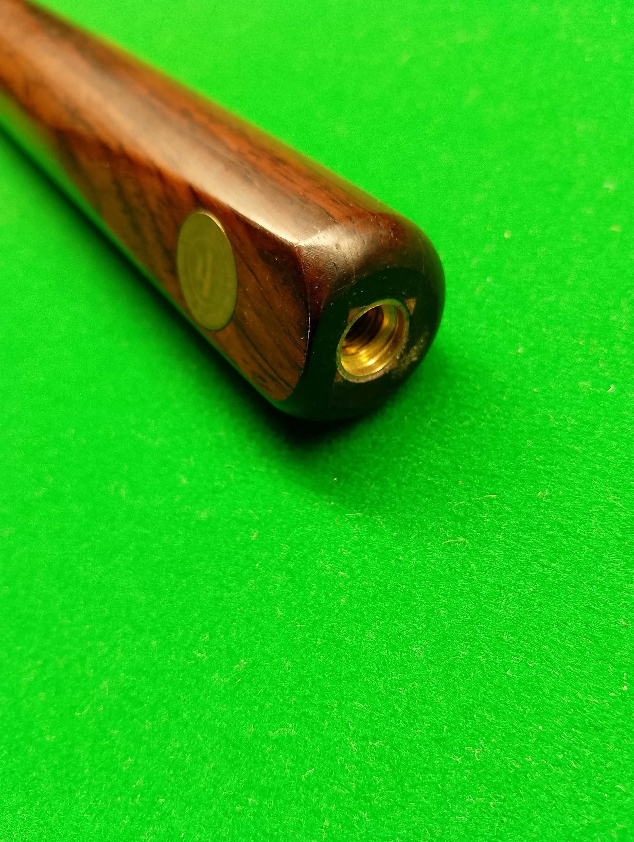 Close-up of a cue stick with a brass insert on a green felt billiards table.