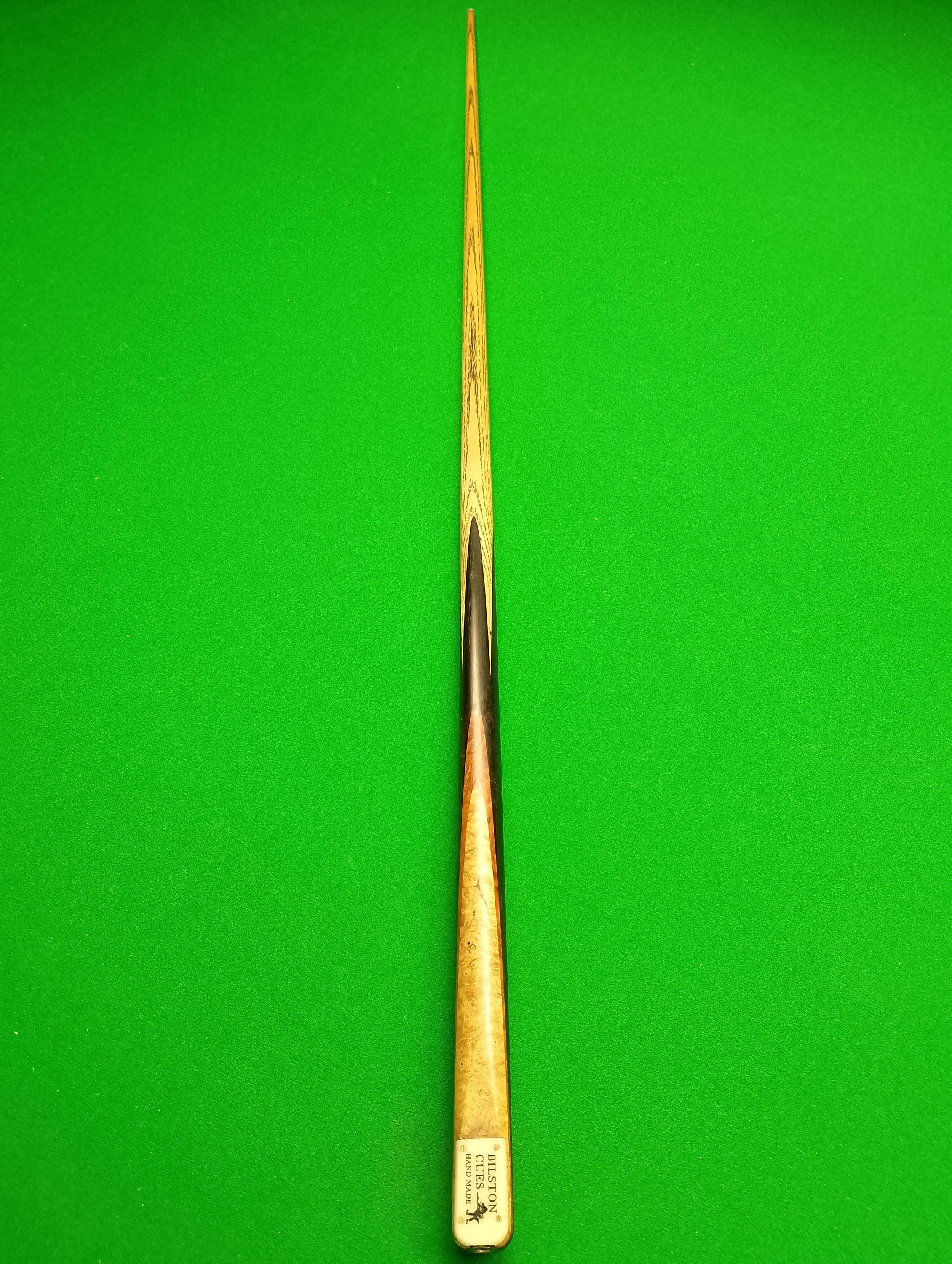 A wooden billiard cue stick placed vertically on a green pool table surface.