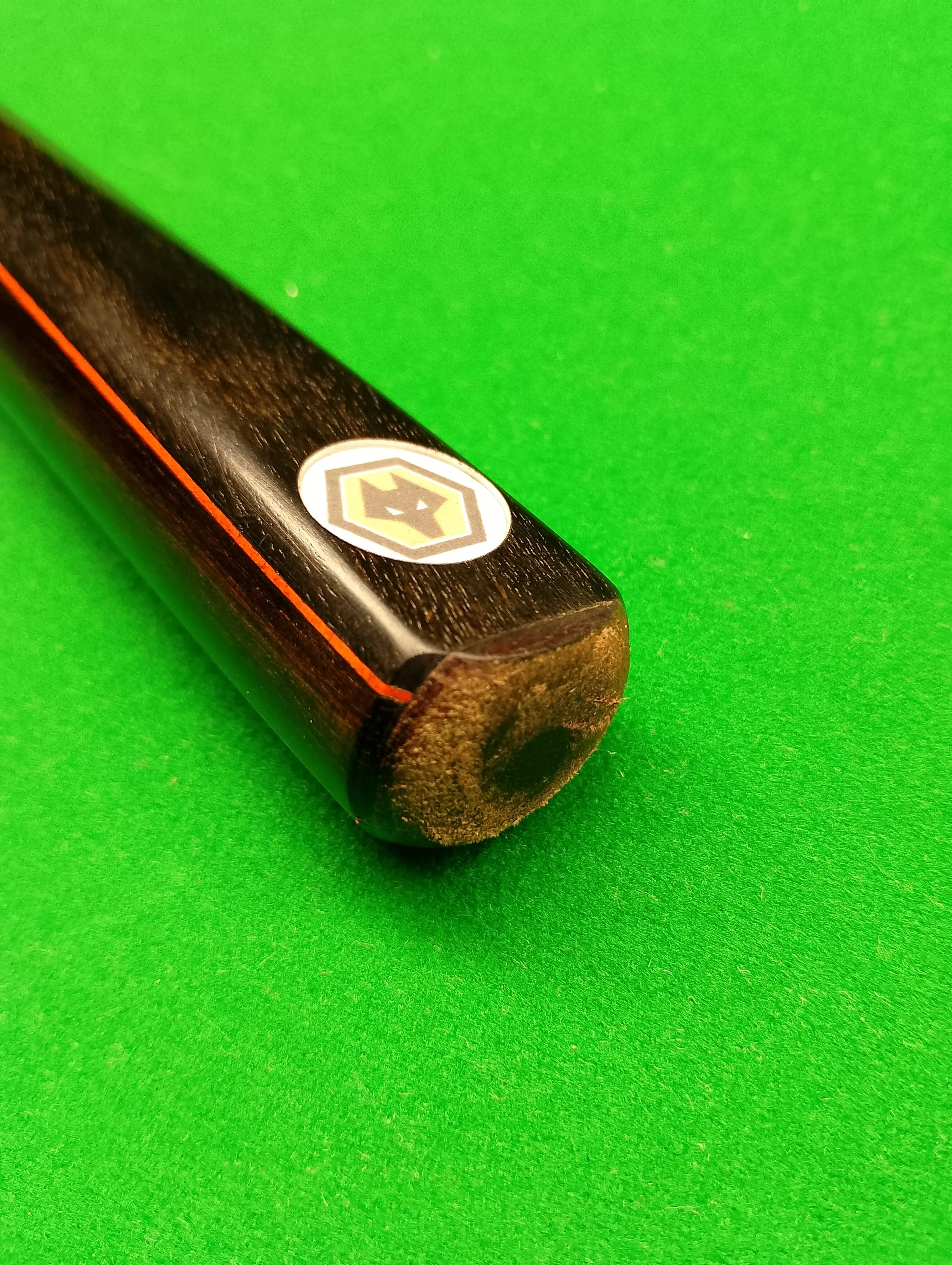 Close-up of a billiard cue stick on a green pool table with a logo near the end.