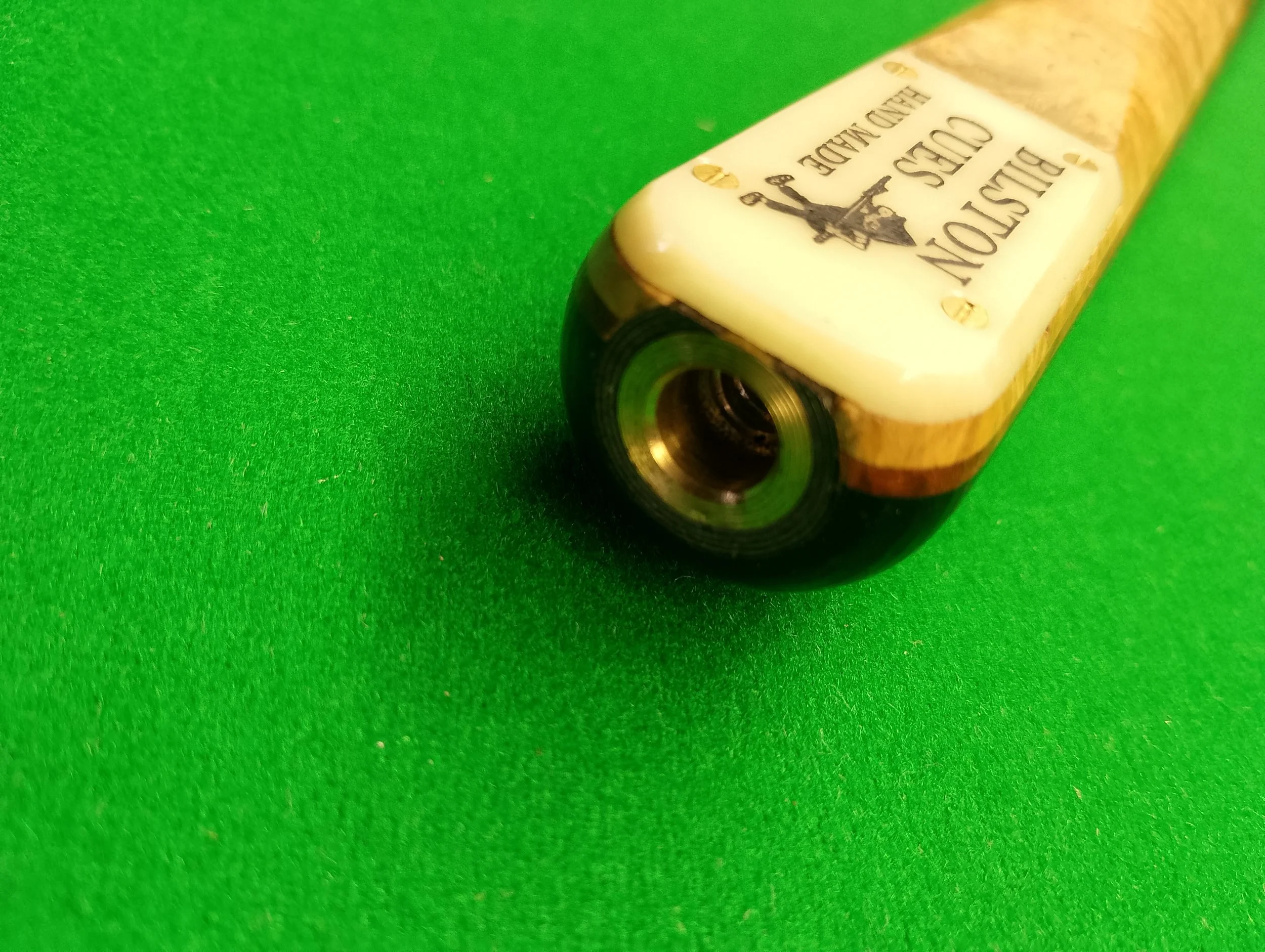 Close-up of a vintage billiards cue chalk container on a green pool table, showing the bottom side with threaded opening.