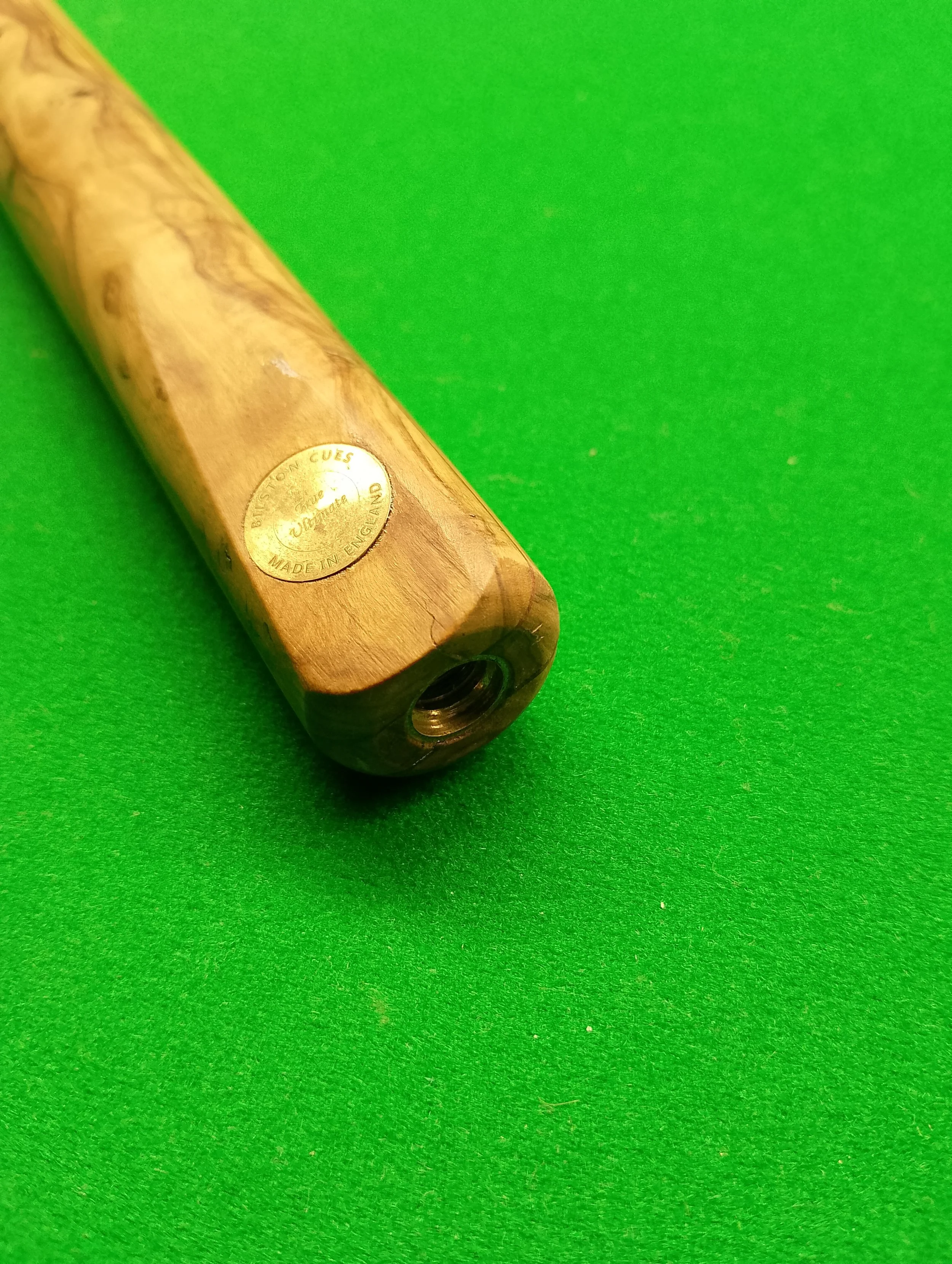Close-up of a wooden billiard cue with a metal logo on a green felt pool table.