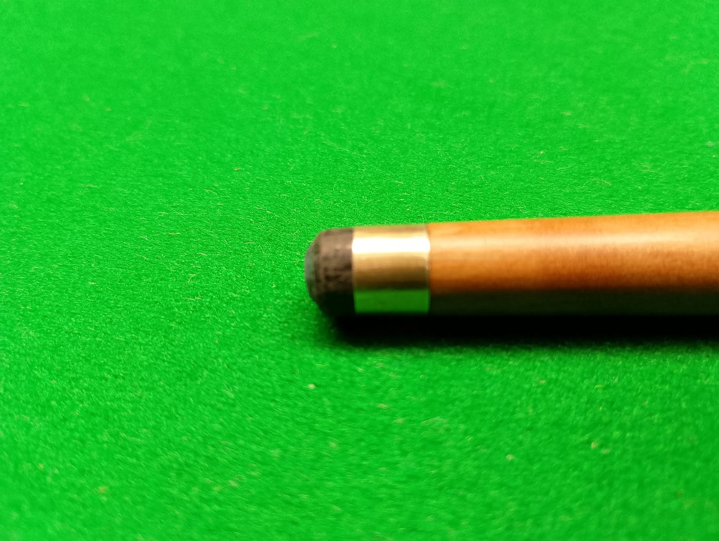 Close-up of a cue stick tip on a green pool table surface.