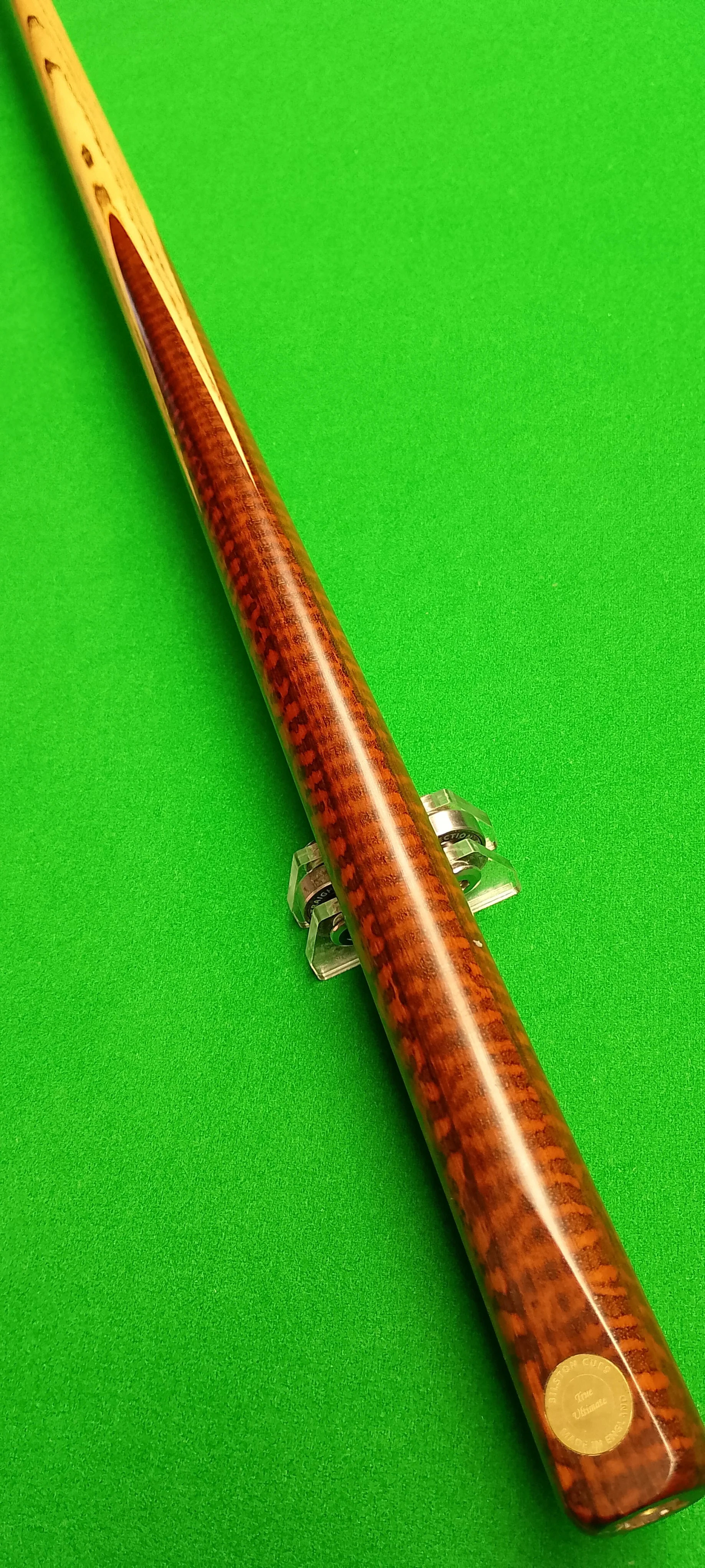 A snooker cue with a cherry wood finish on a green pool table surface.