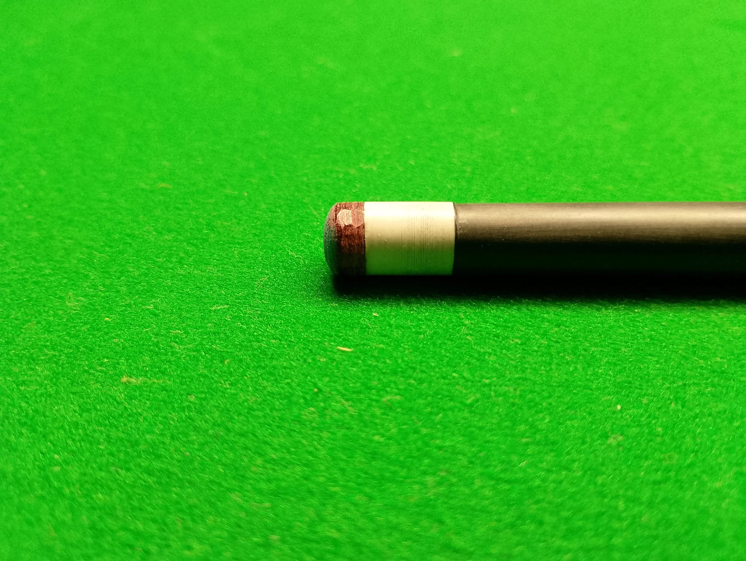 A close-up of a cue stick tip resting on a green pool table surface.