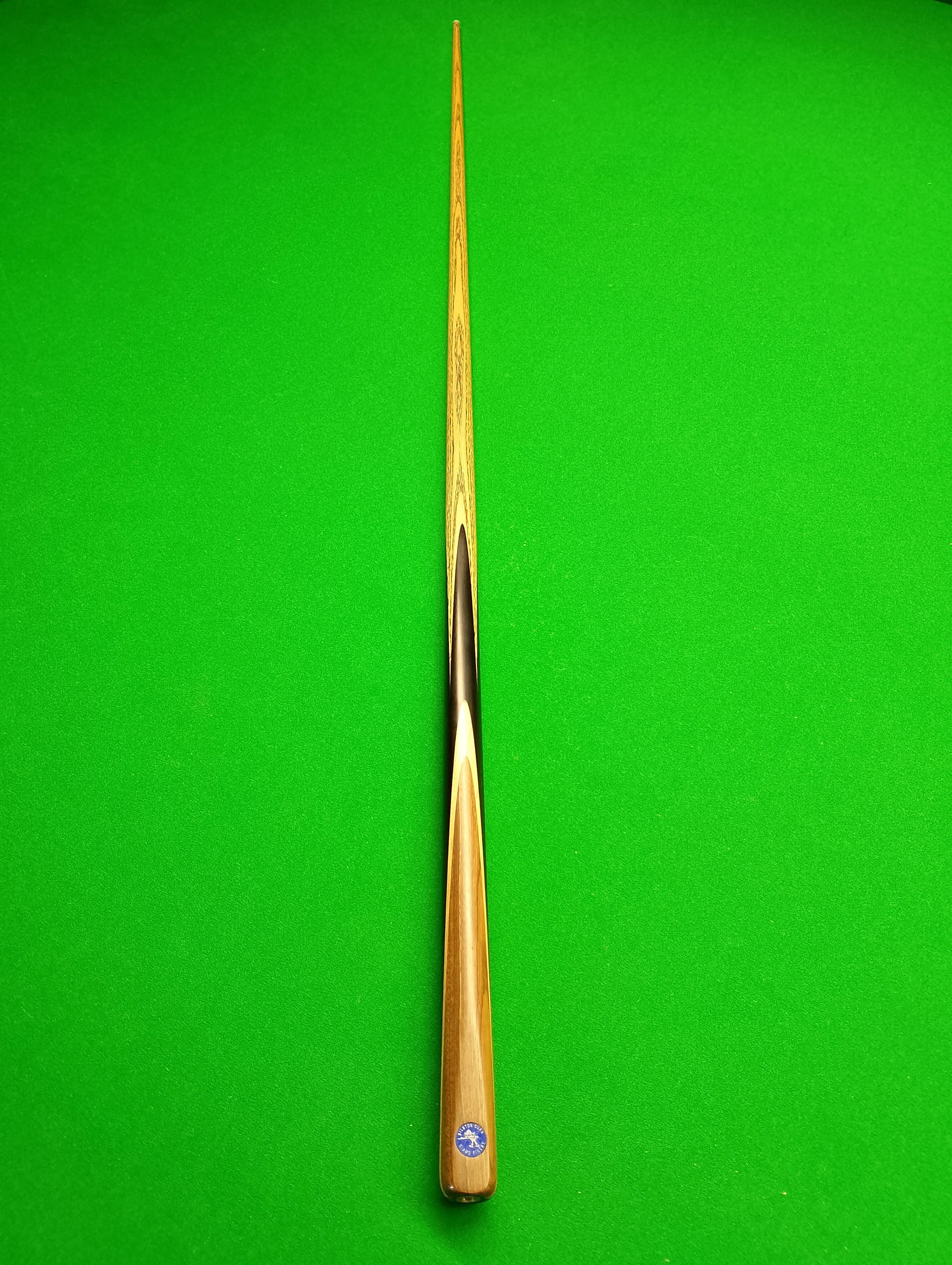 A wooden cue stick for billiards or pool resting on a green felt table.