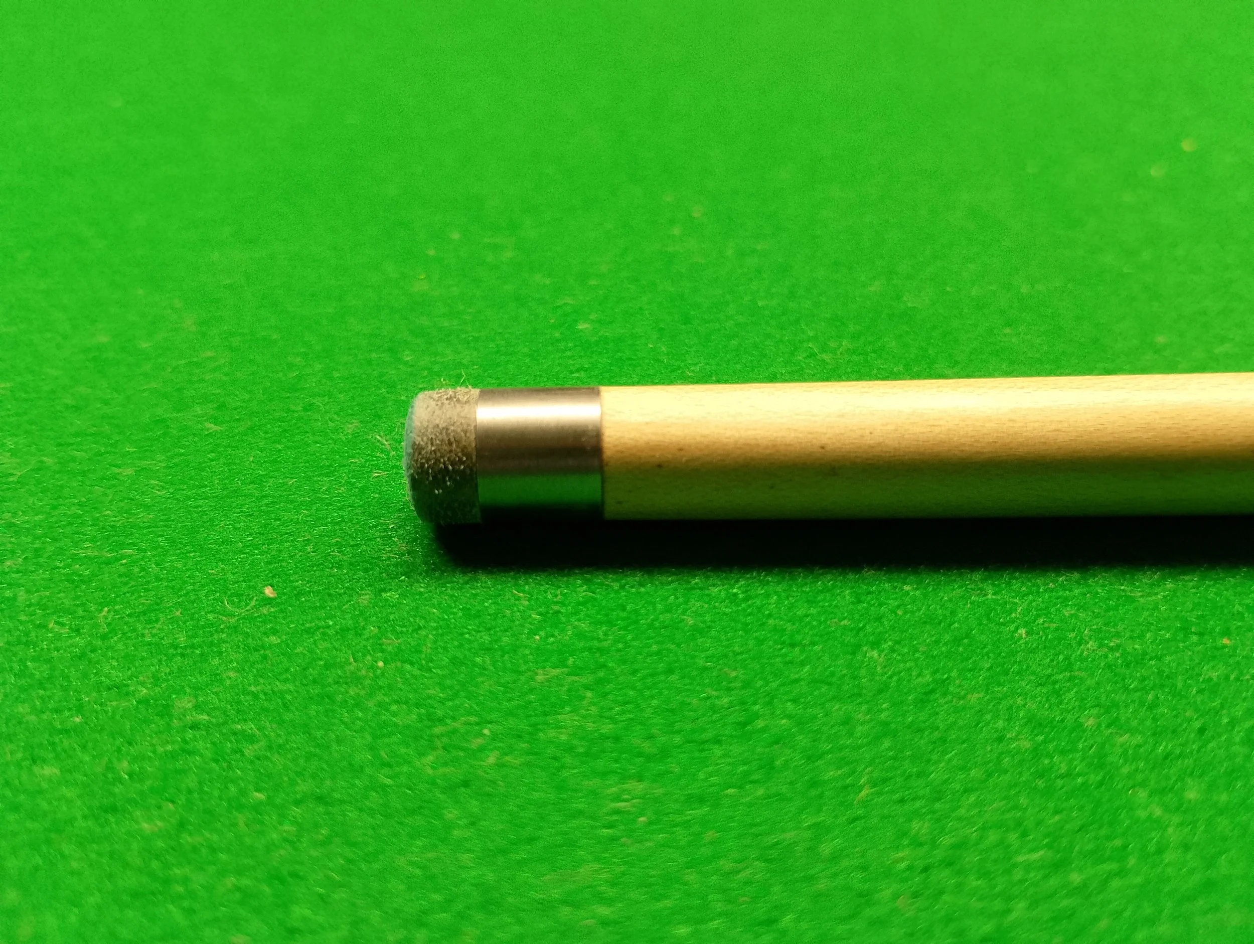 Close-up of a pool cue tip resting on a green pool table felt.